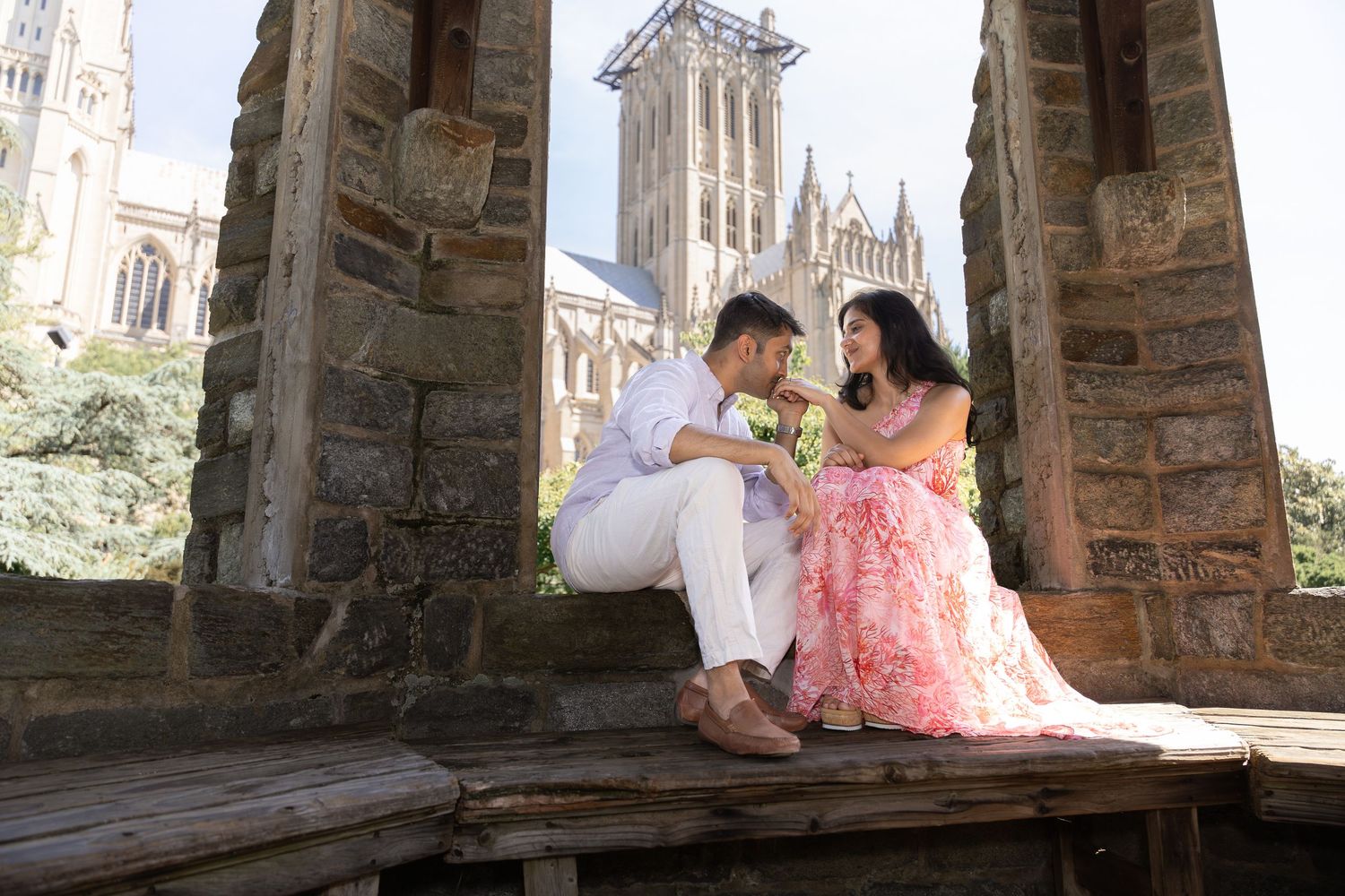 A couple sits together in a romantic stone archway overlooking a Gothic church tower on a sunny afternoon.