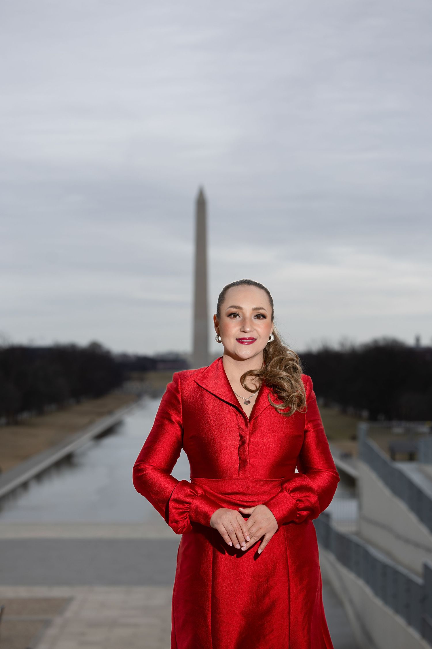 Bold red coat dress styled against Washington Monument backdrop on cloudy day.