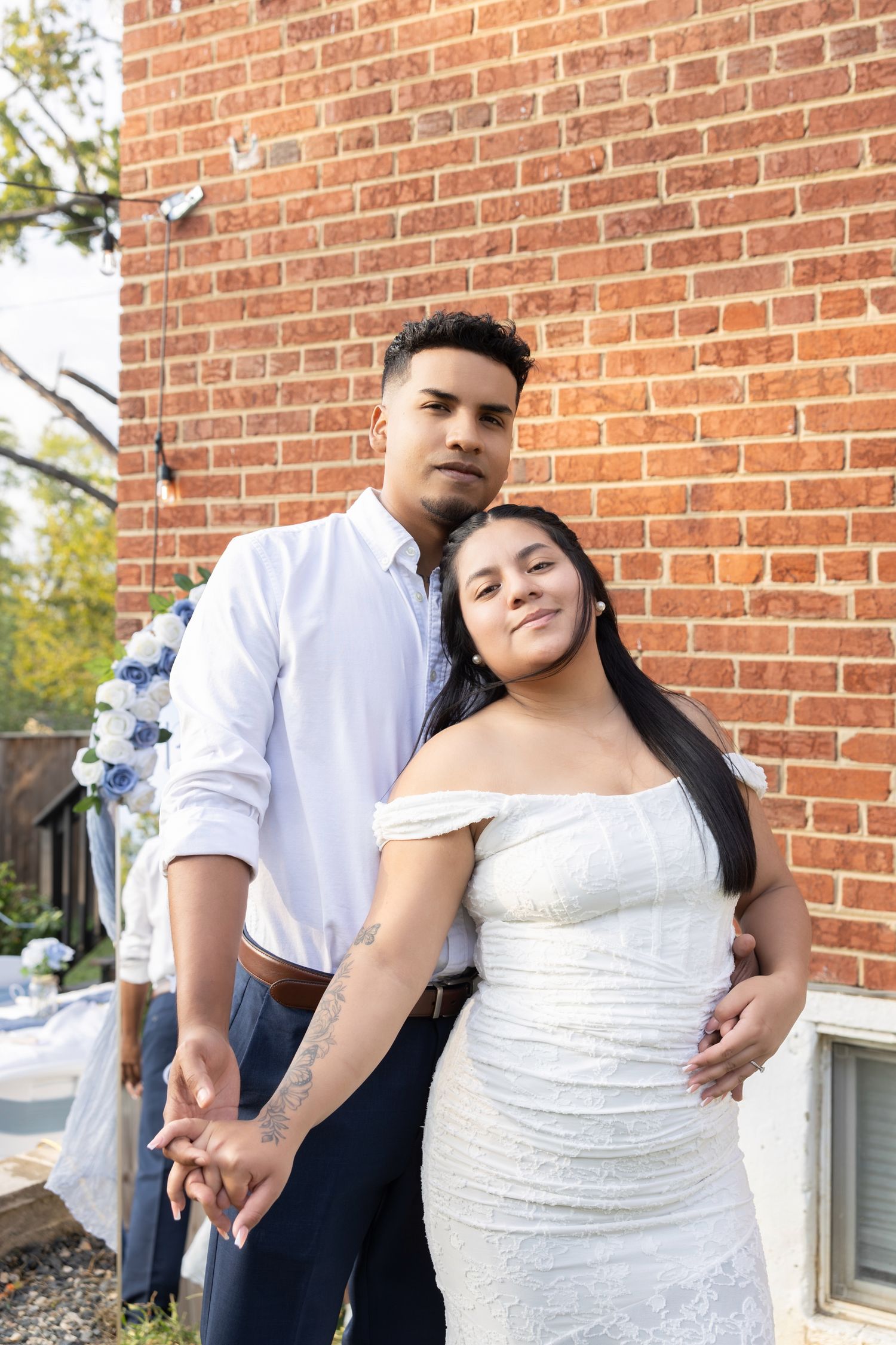 A couple in wedding attire pose together against a red brick wall in a series of romantic outdoor photos.