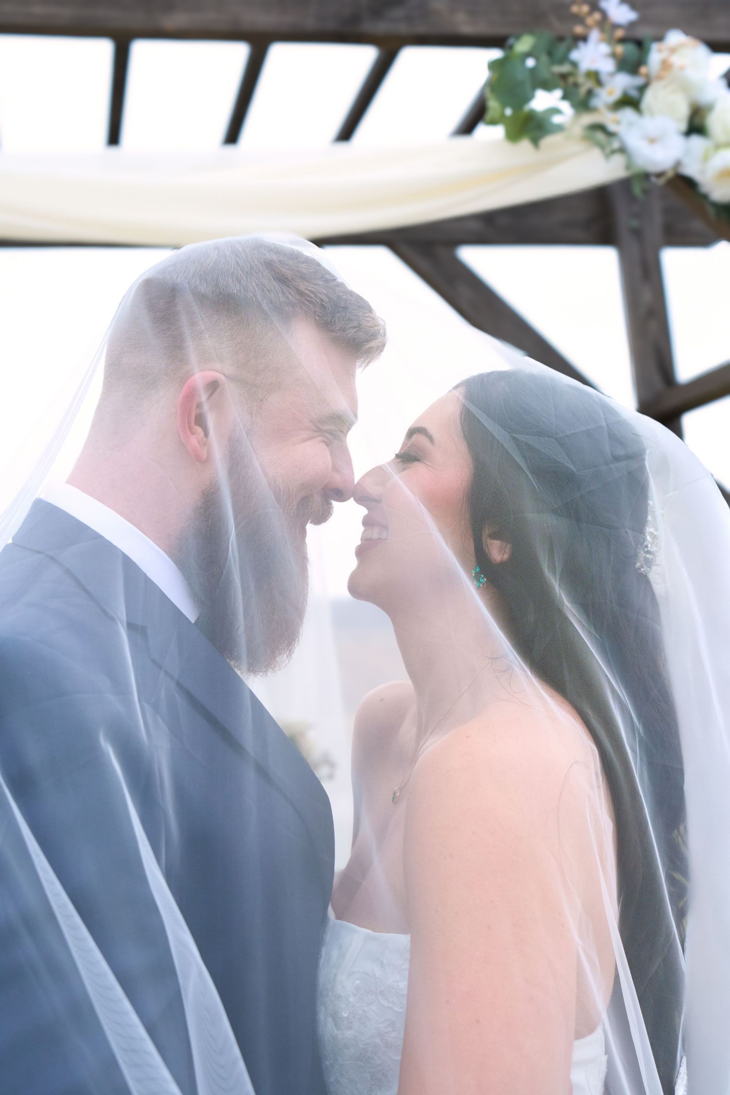 Intimate moment between newlyweds sharing laughter under a pergola with soft lighting.