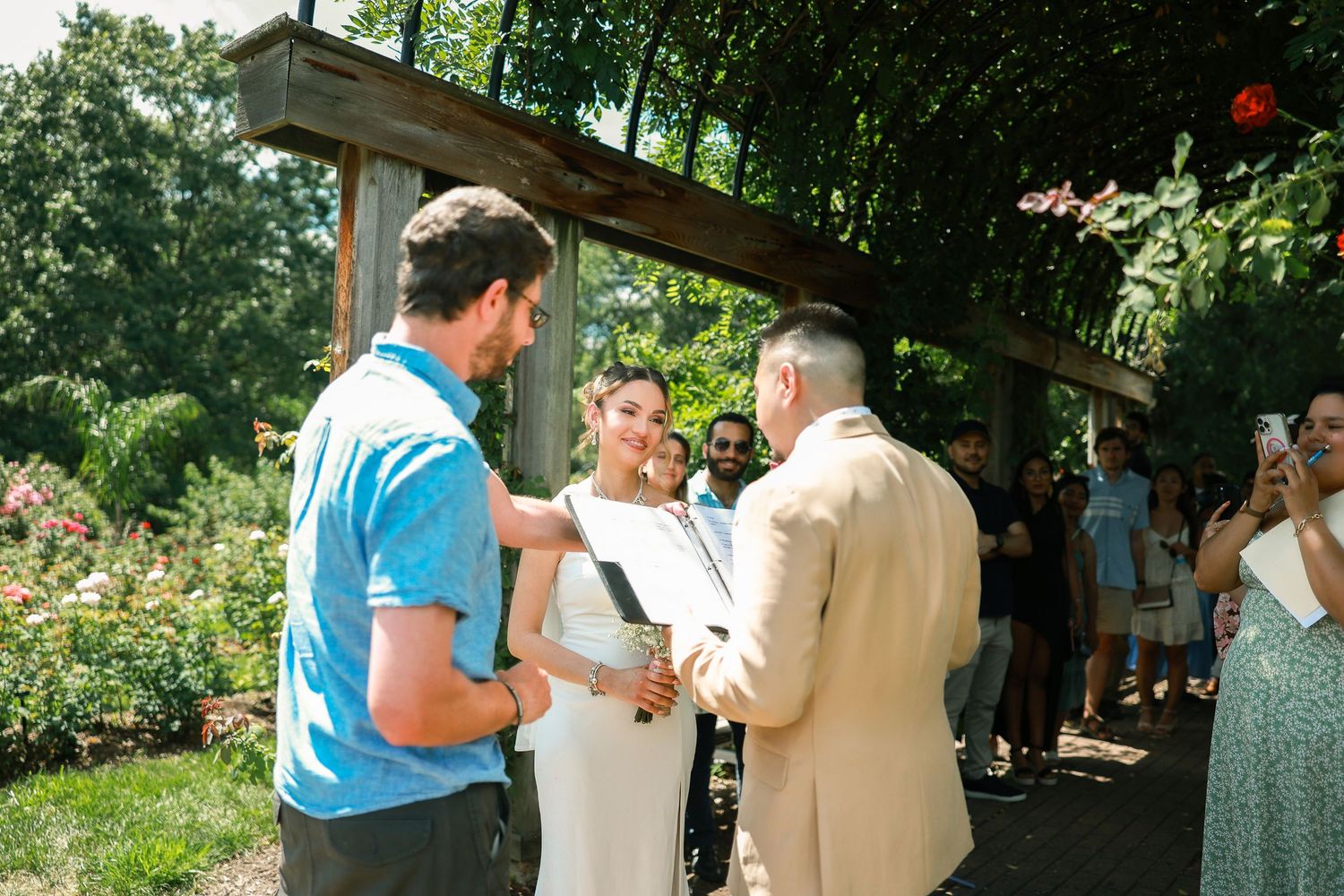 Wedding party gathered under a shaded outdoor pavilion during summer celebration.