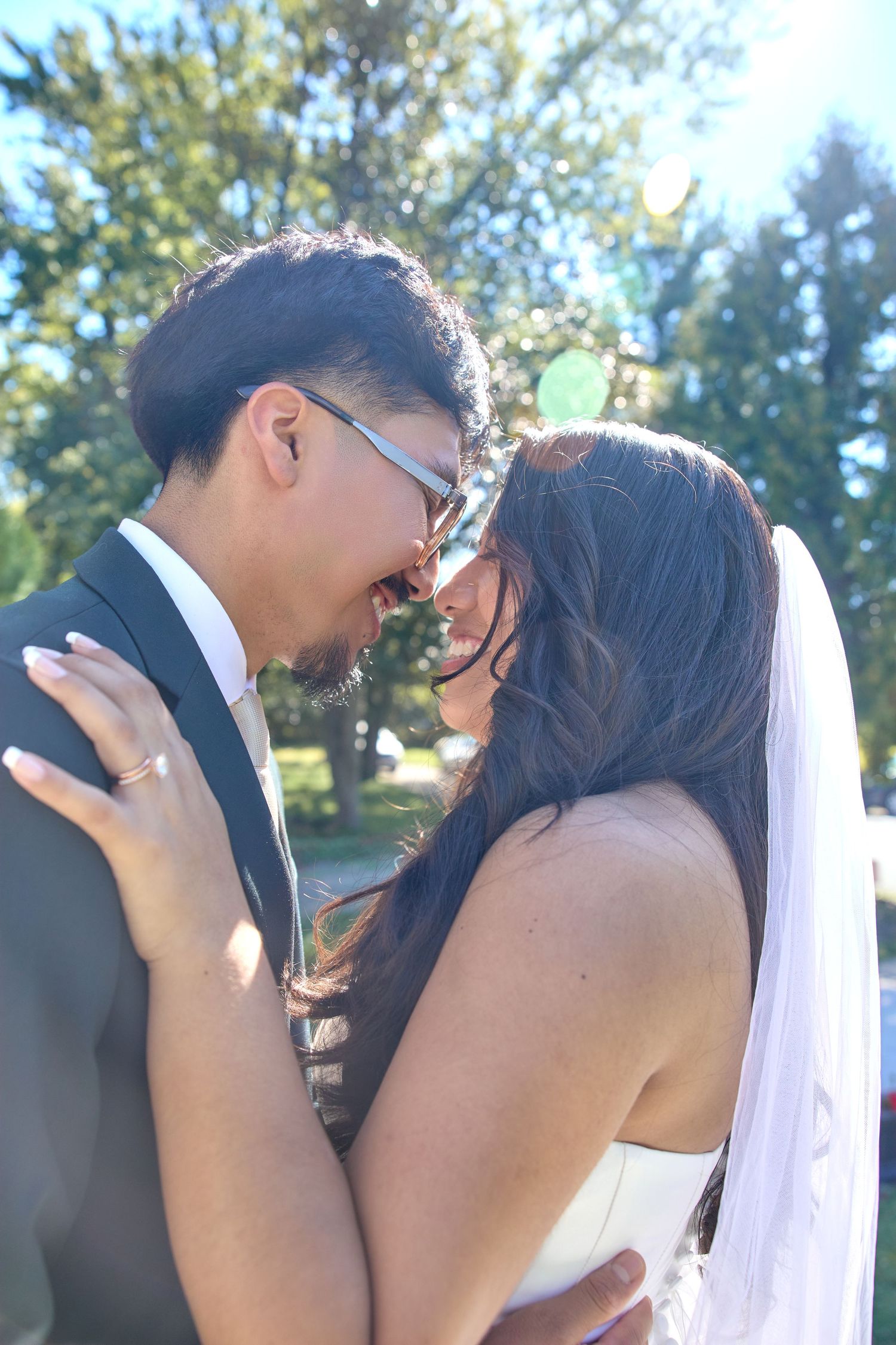 Romantic wedding couple shares an intimate moment under sunlit trees during their ceremony.