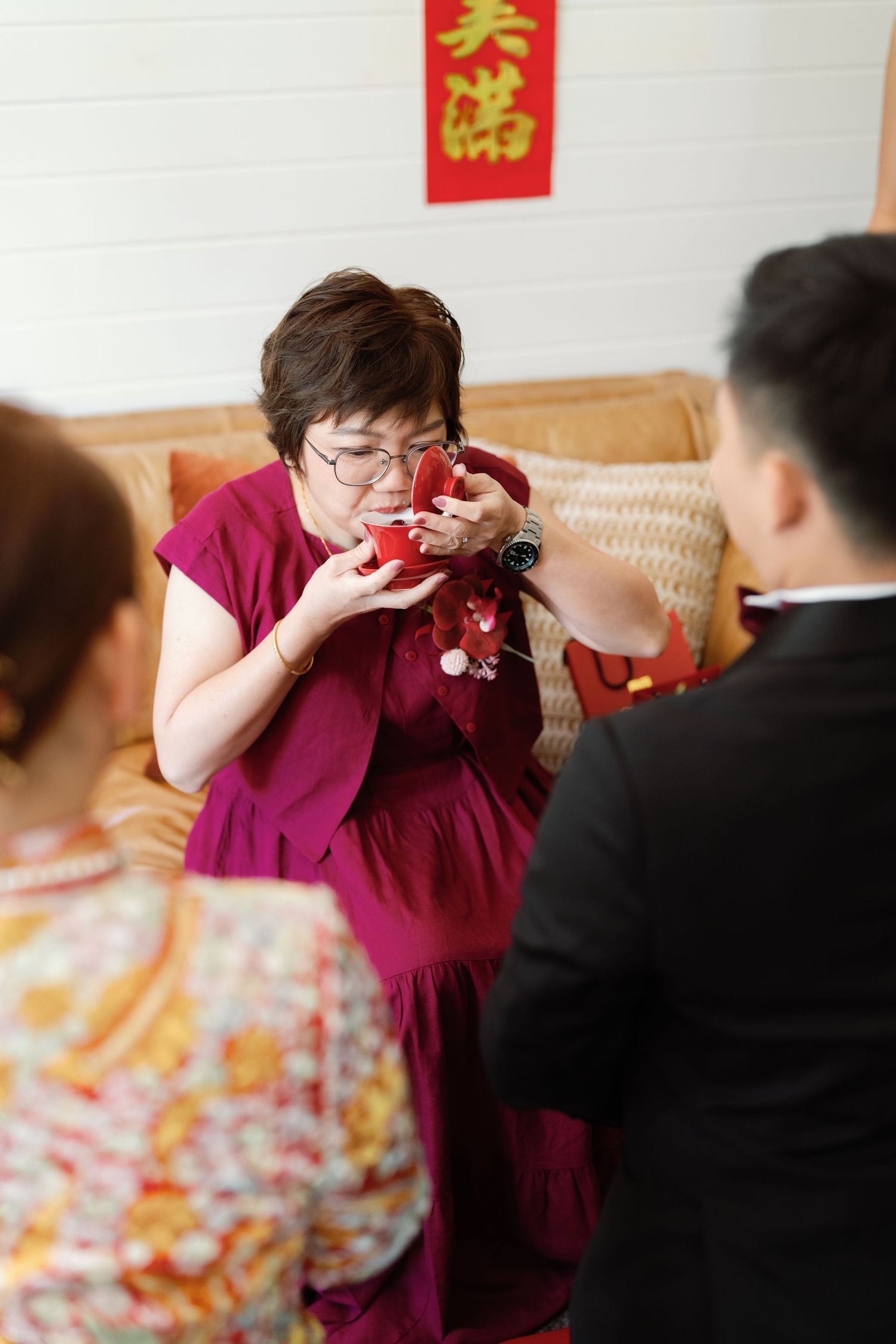 Woman in burgundy dress reacts emotionally during traditional Chinese tea ceremony.