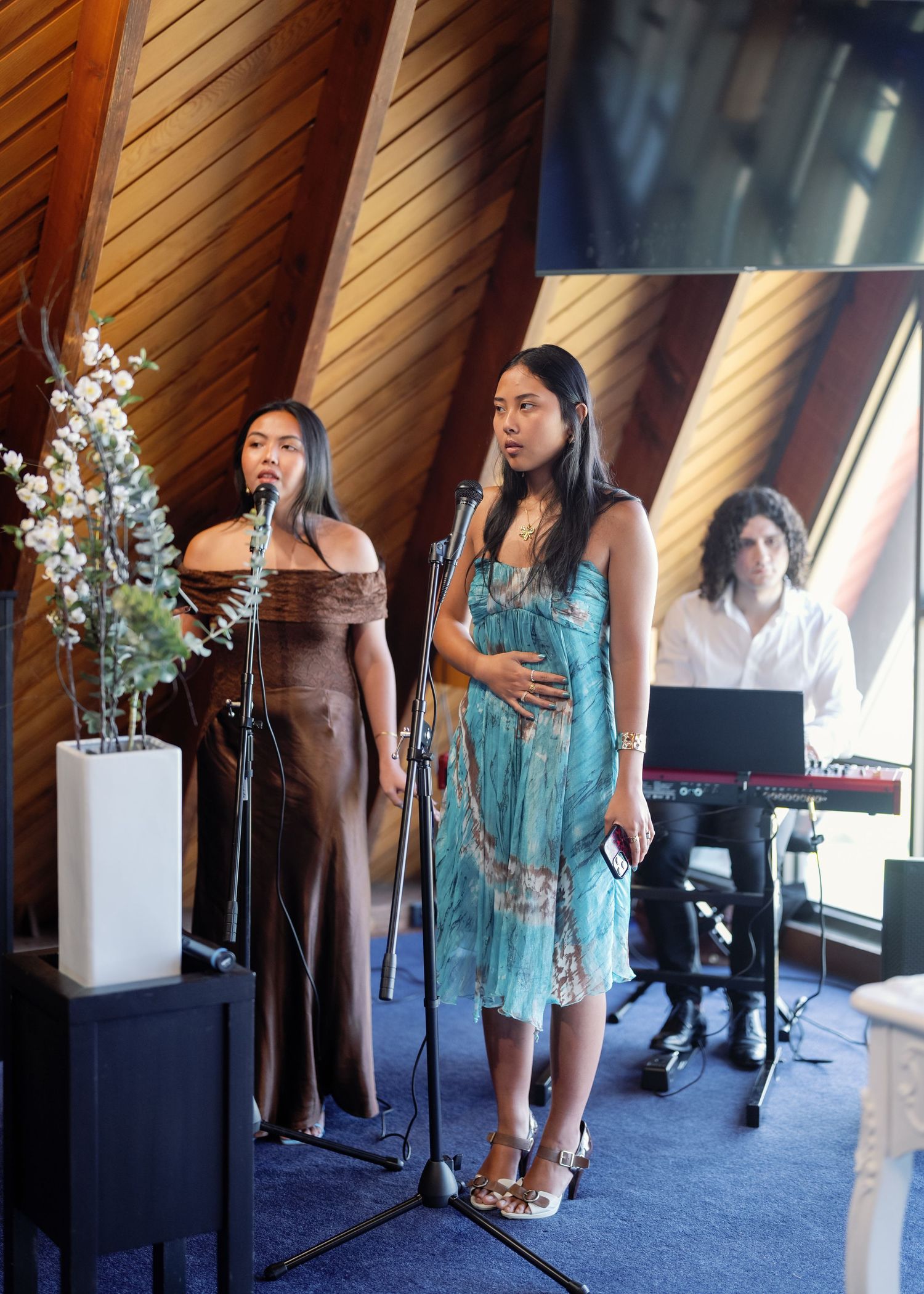 Wedding party members in turquoise dresses dance together on a carpeted floor with wooden ceiling beams.