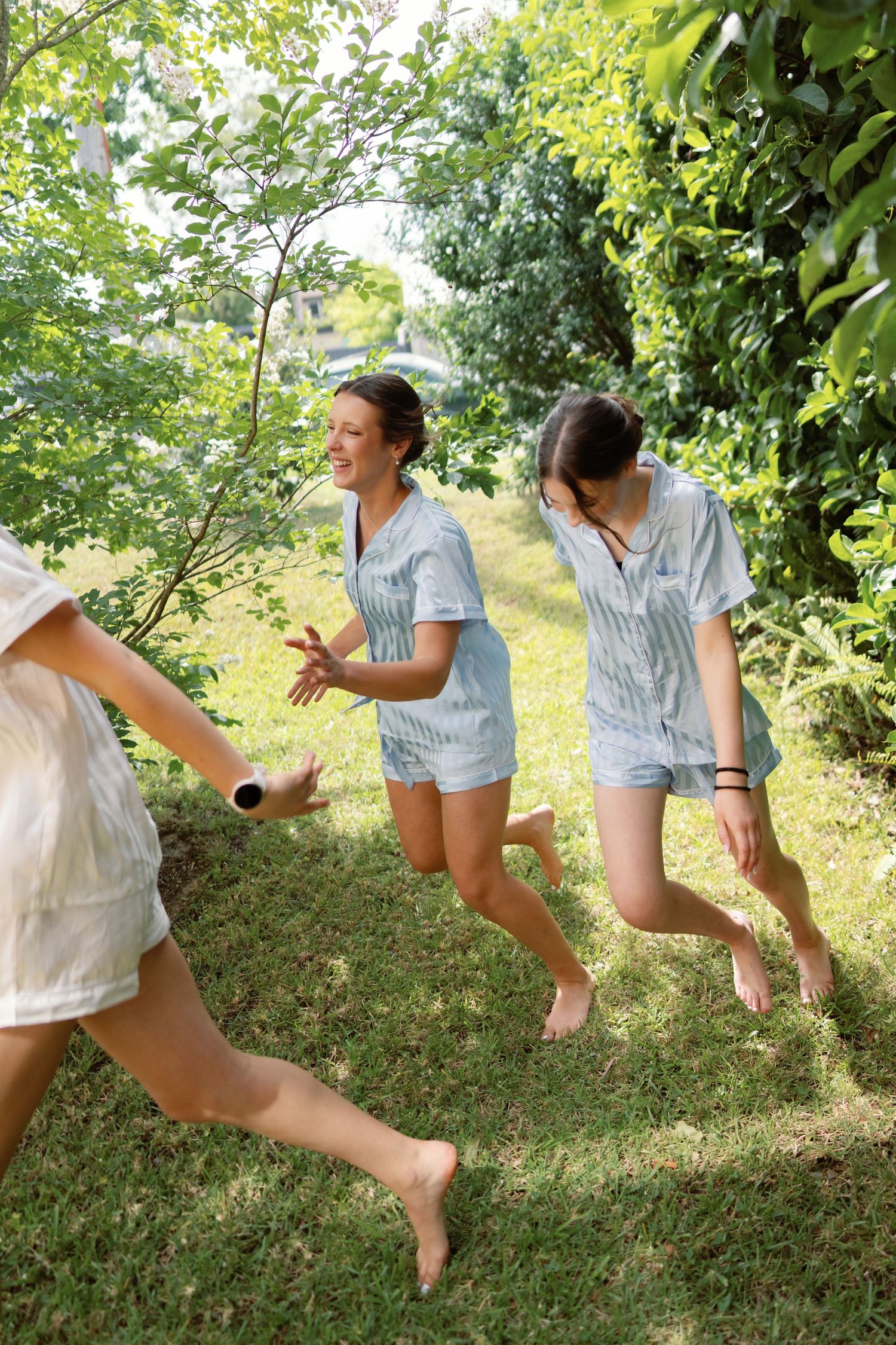 People in coordinated outfits jump joyfully on a grassy hillside under green trees.