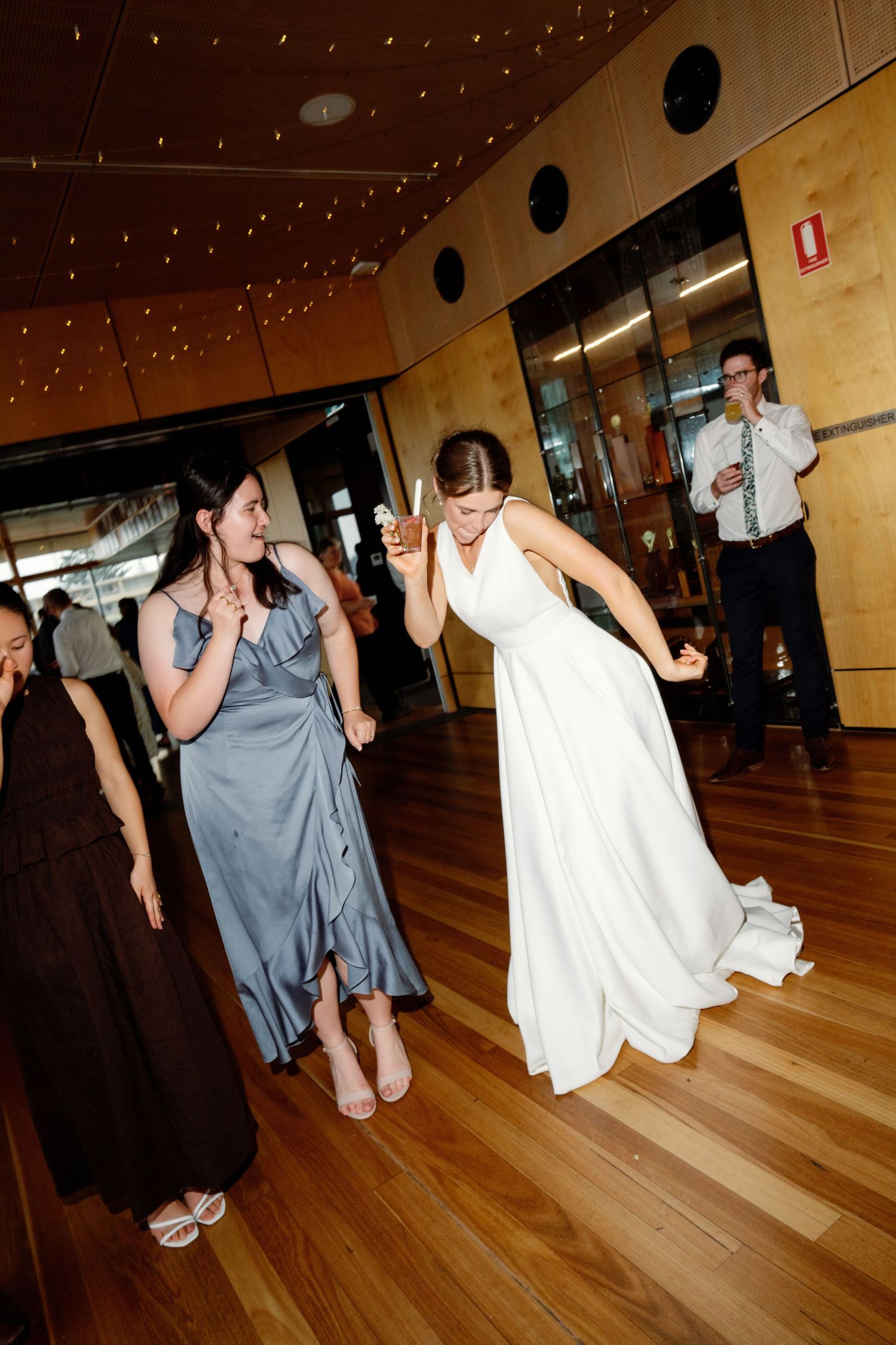 Wedding party dancing and celebrating on a polished wooden floor in an indoor venue.