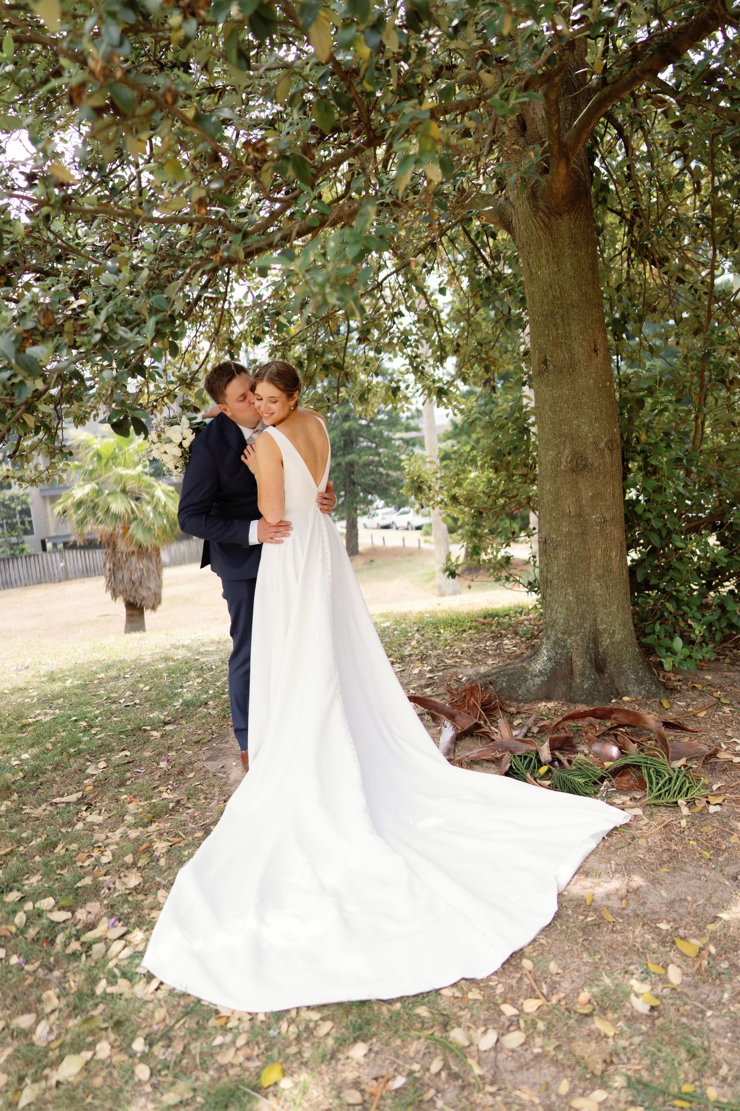 A romantic wedding photo series showing a couple in a white dress and navy suit embracing under trees in an outdoor setting.