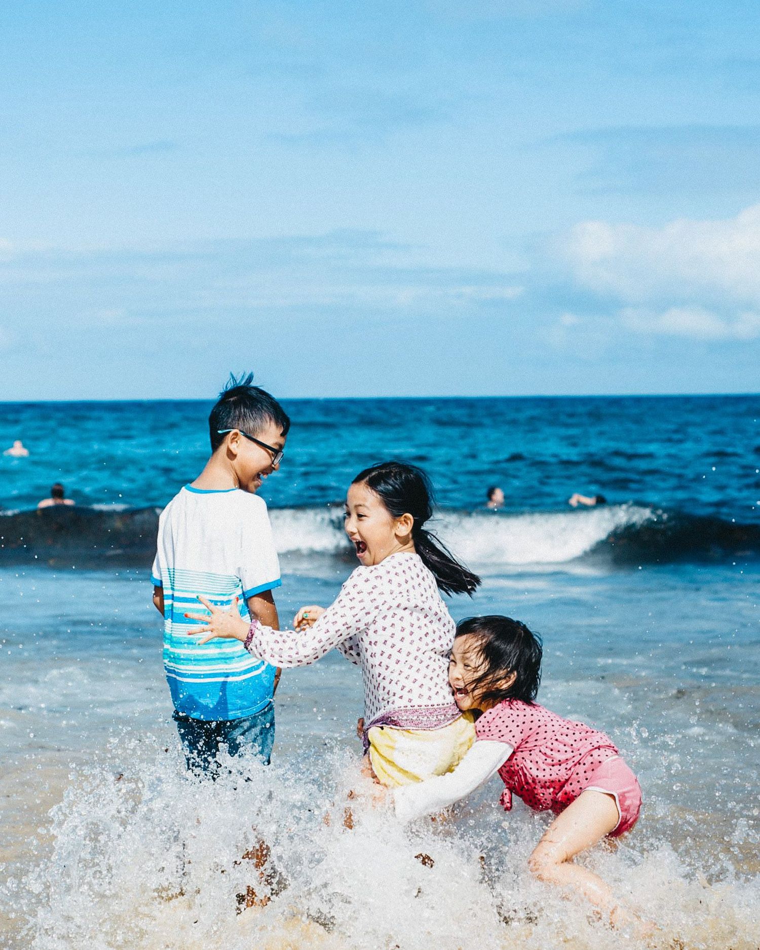 Children playing and splashing in ocean waves on a sunny day at the beach.