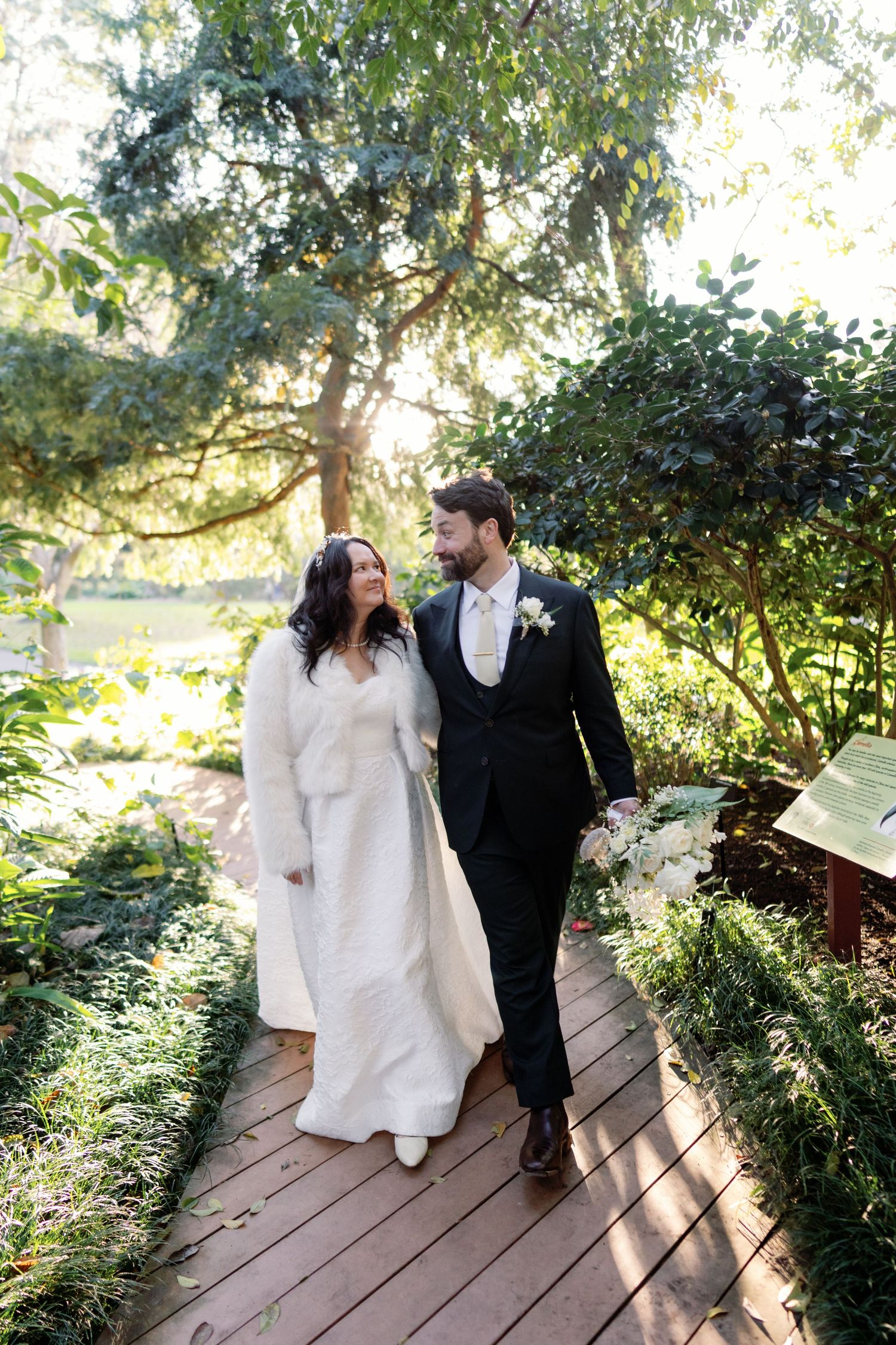 Couple sitting together on a rustic wooden bridge surrounded by lush greenery in a romantic garden setting.