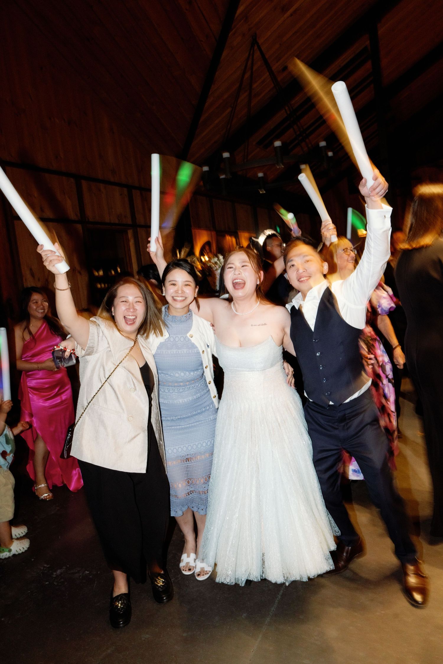 Wedding celebration with guests dancing and raising their arms in joy at a dimly lit reception venue.