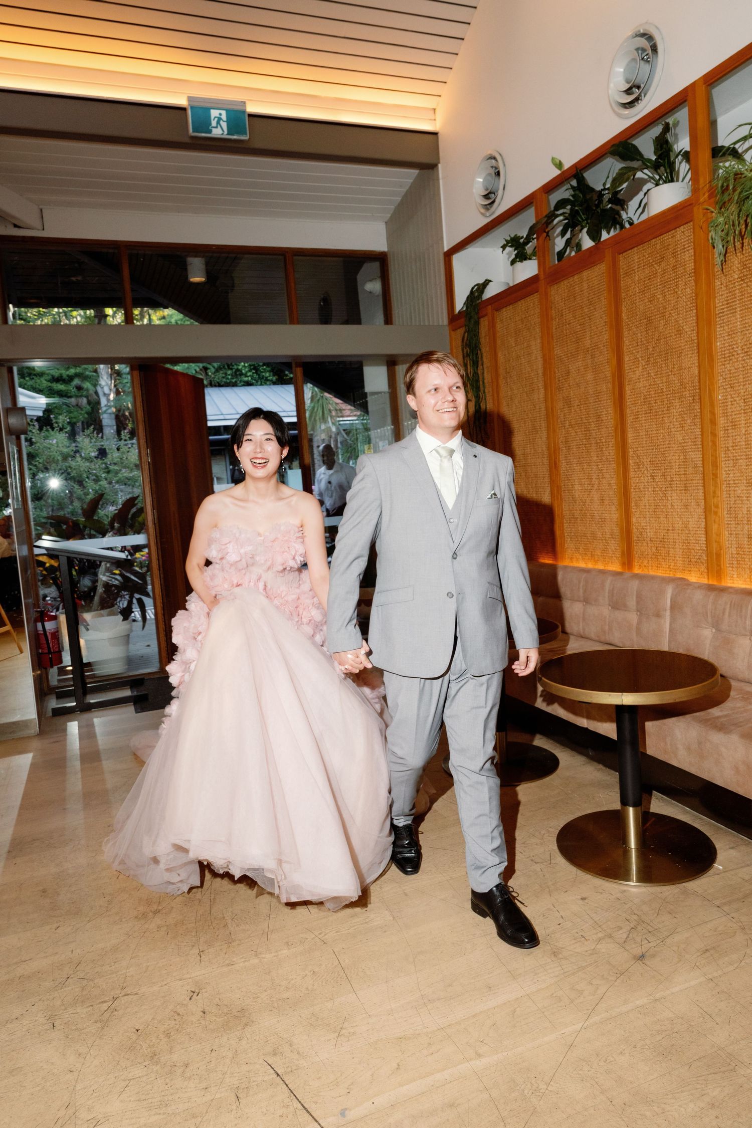 Wedding couple walking through indoor venue with wood paneled walls.