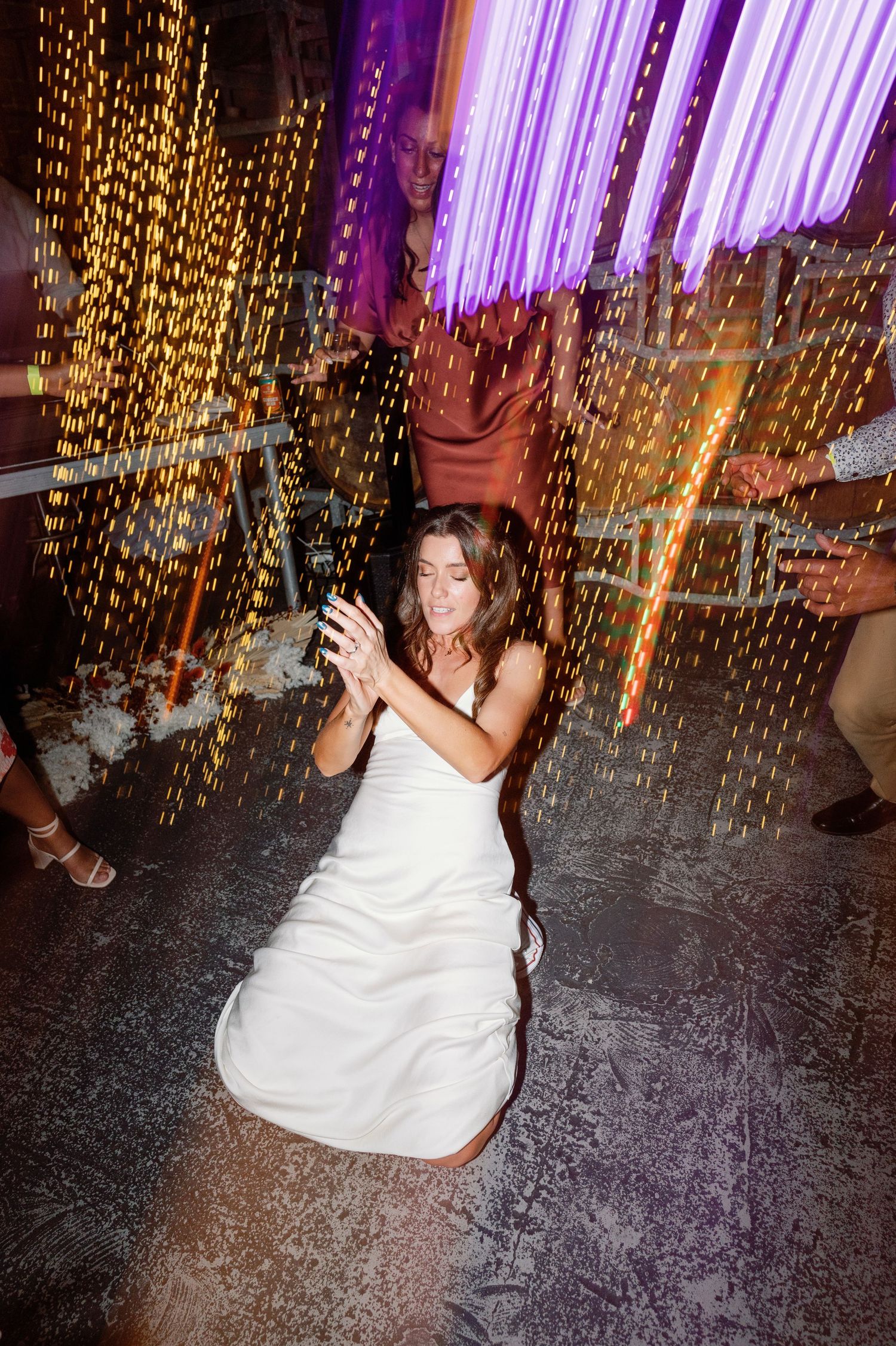 People dancing under purple and gold string lights at a wedding reception.