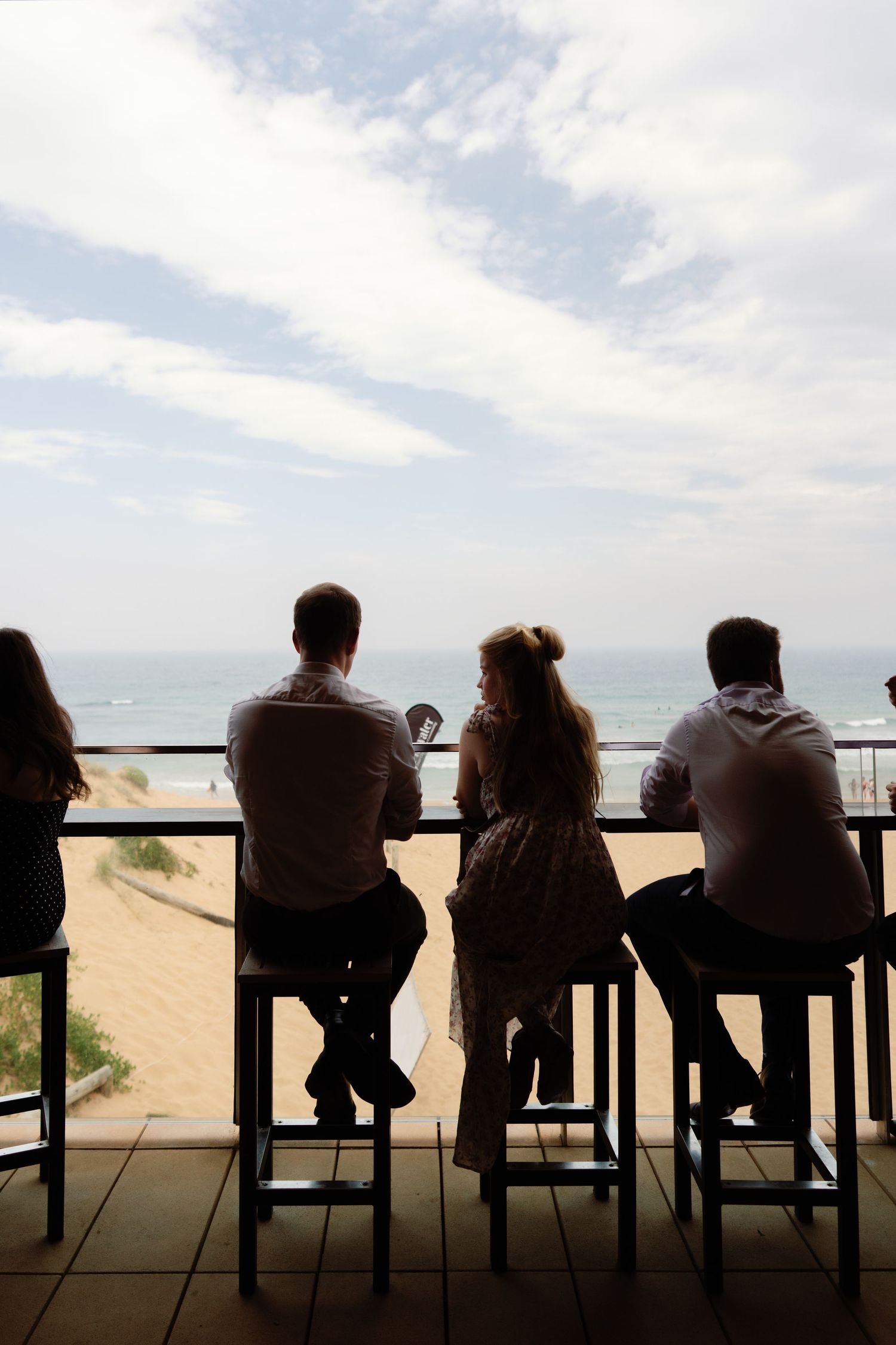 Silhouettes of people sitting on chairs against dramatic beach and sky backdrop.