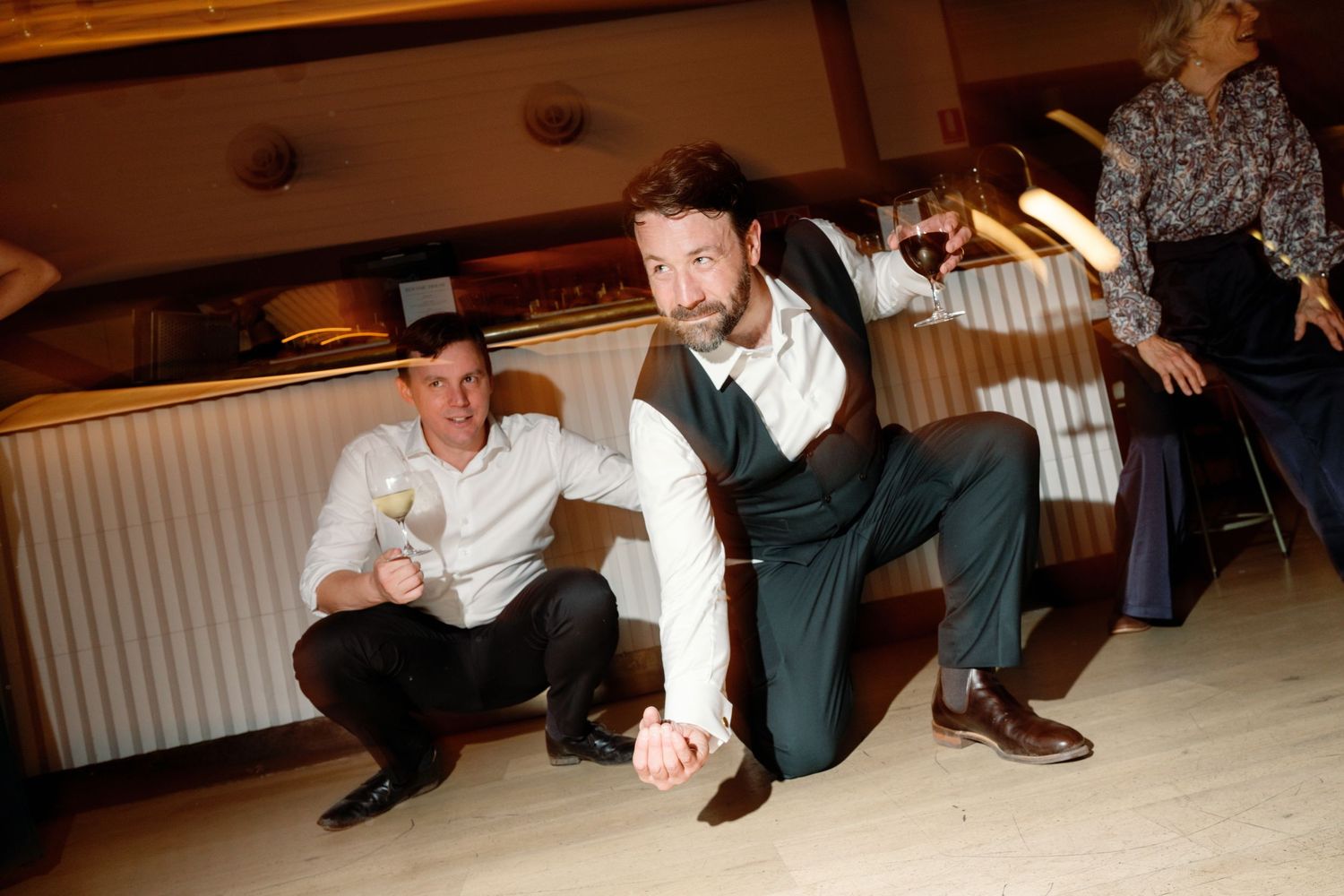 Man energetically dancing on a dance floor while guests watch and enjoy drinks at a wedding reception.