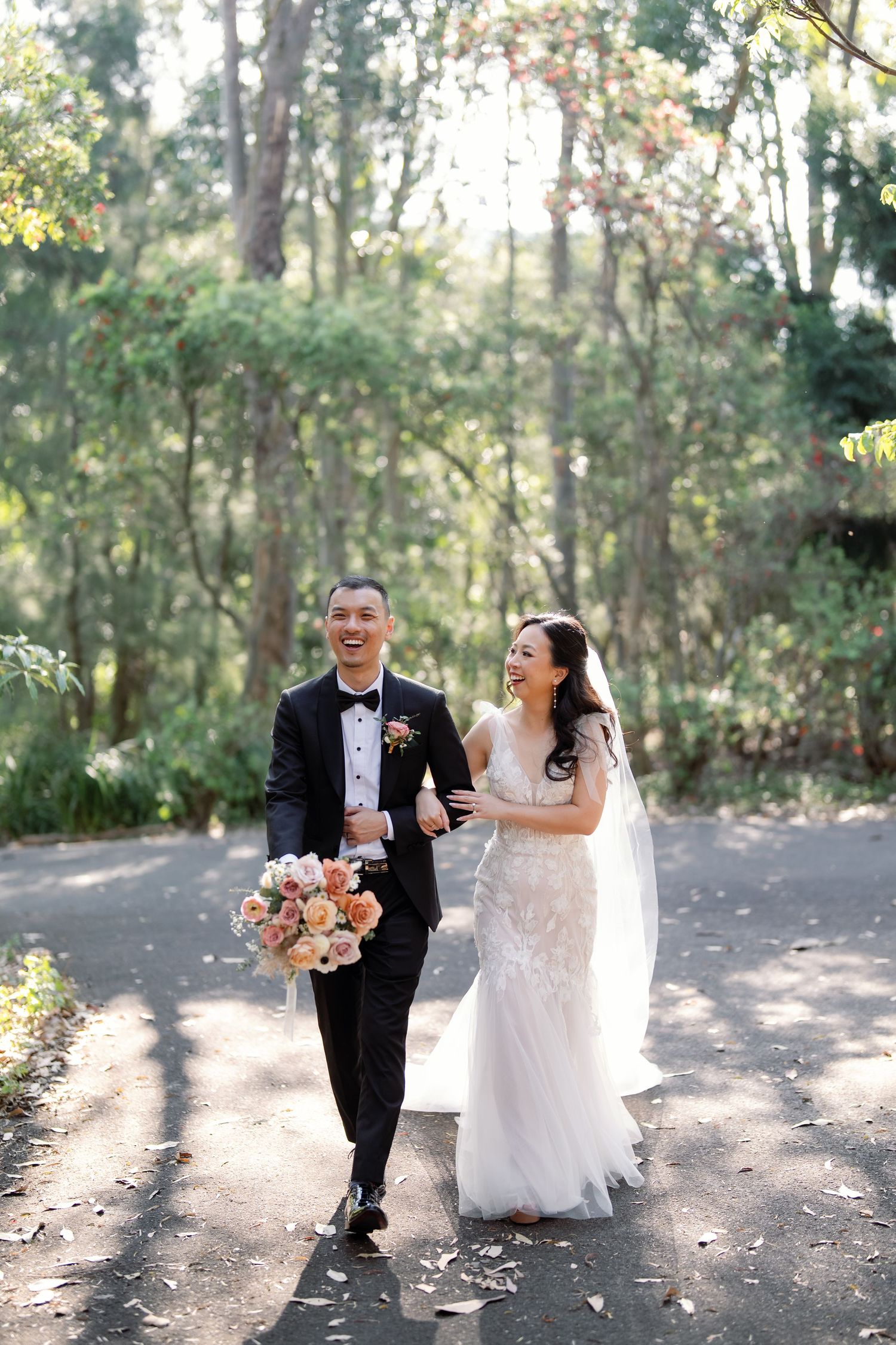 Bride and groom walking together on a sunlit forest path.