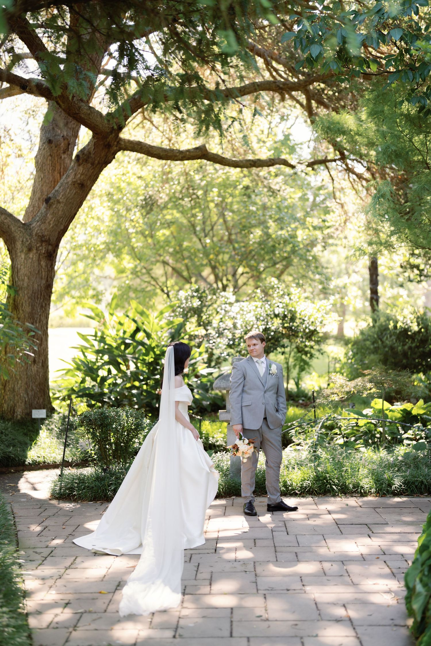 Wedding couple poses for romantic portraits in a sunlit garden with stone pathways.