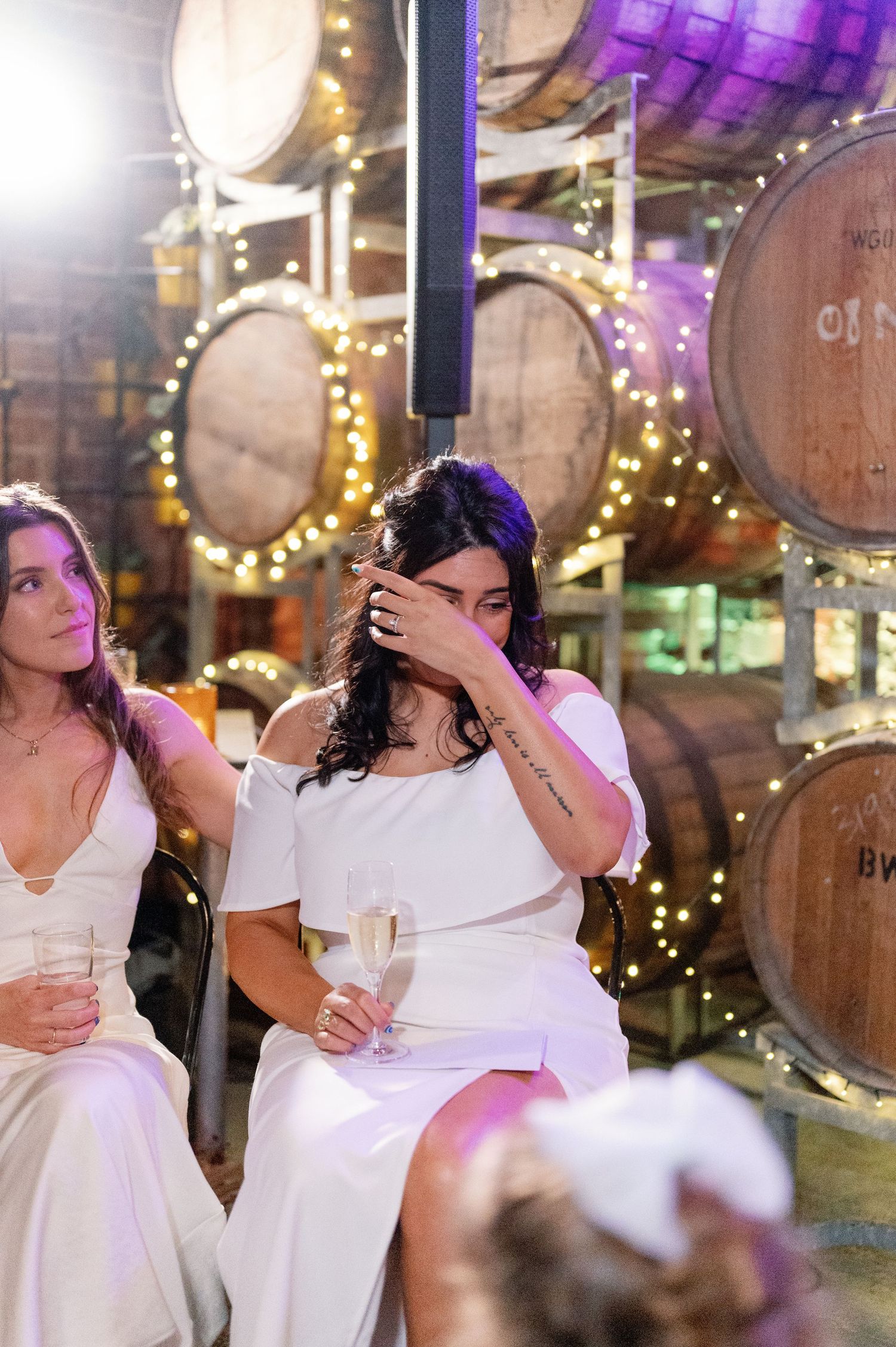 Wedding celebration at a rustic venue with wooden barrels and purple lighting showing candid moments.
