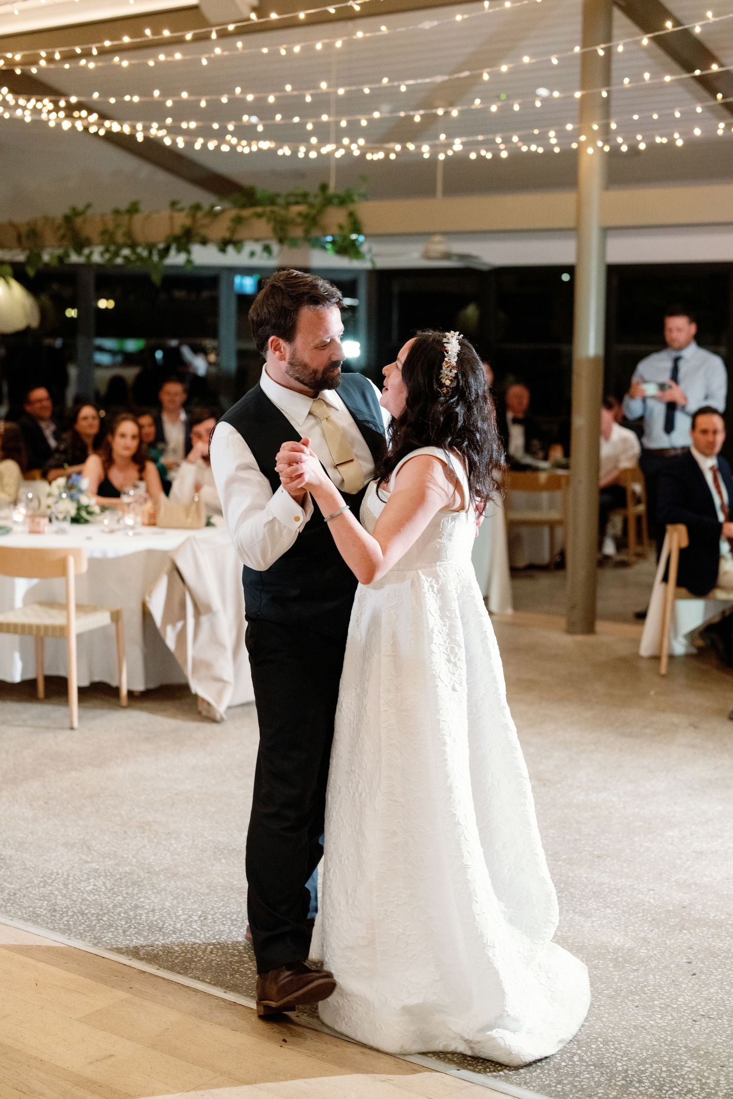 Bride and groom share first dance under fairy lights at elegant outdoor wedding reception.