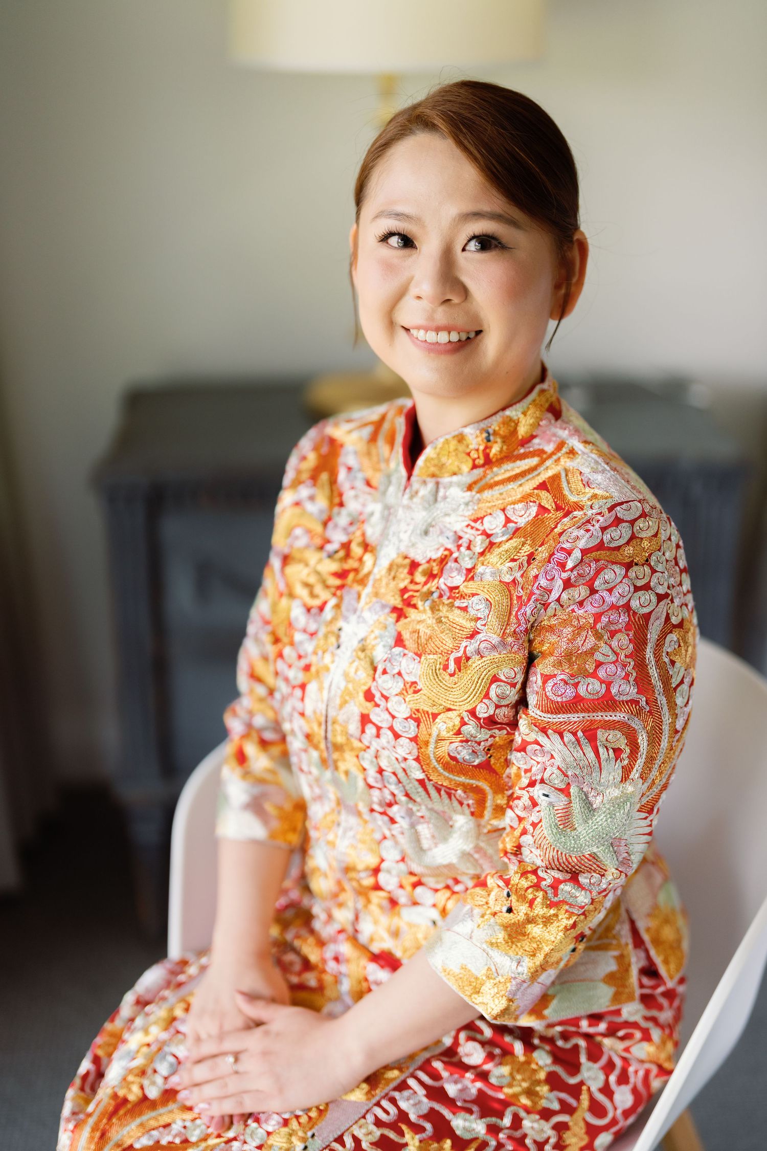 A person wearing a traditional orange and red floral Chinese qipao dress smiles warmly.