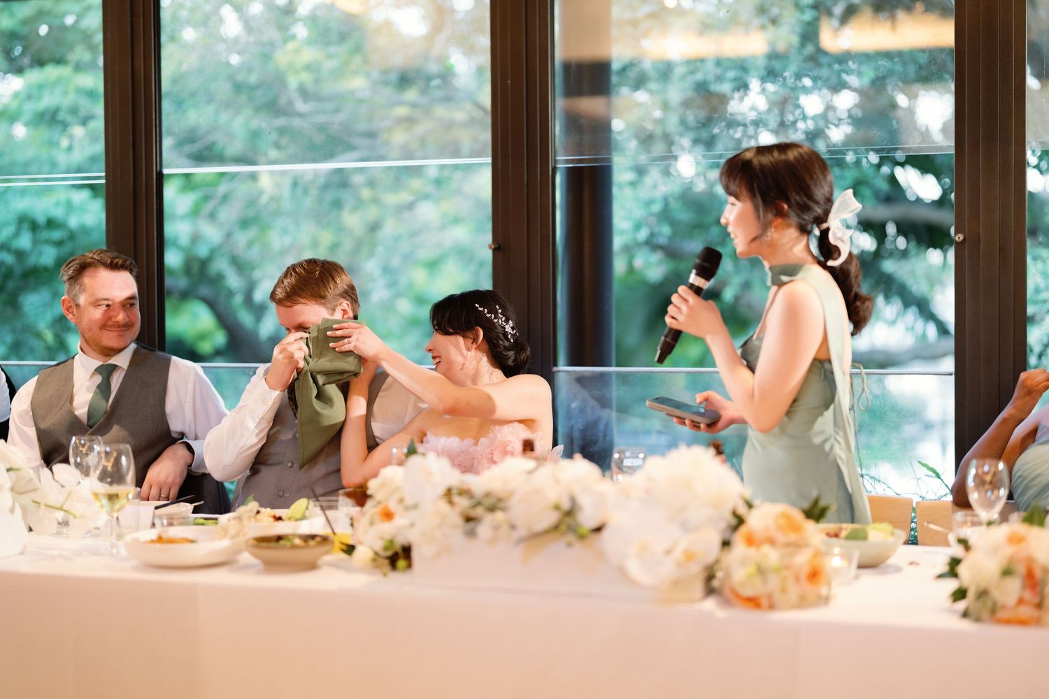 Wedding reception table setting with guests dining in an elegant indoor venue with natural lighting.