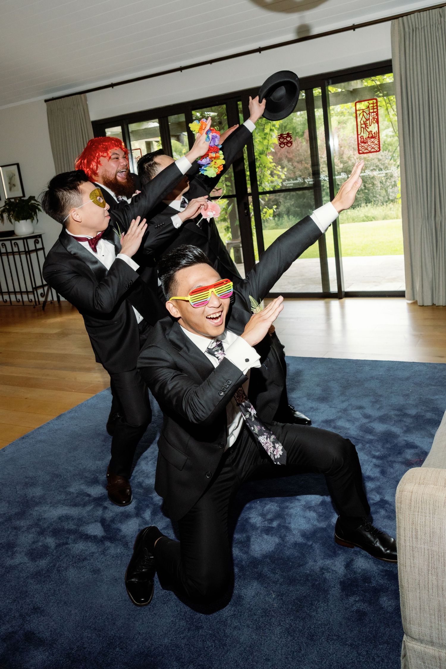 Wedding party members in black suits performing dramatic jumping poses on a blue carpet.