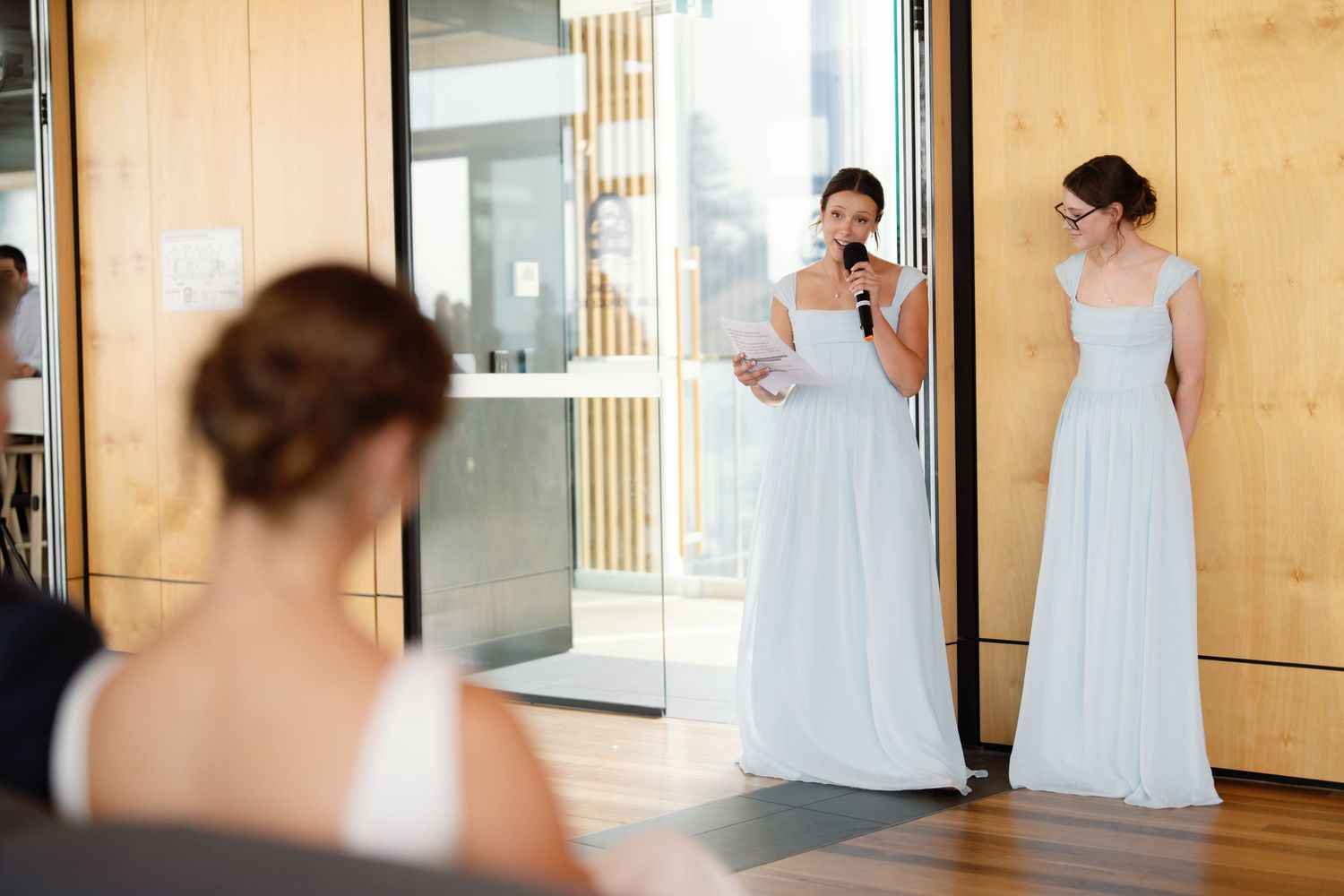 Bridesmaids in pale blue dresses preparing in a modern room with wooden walls.