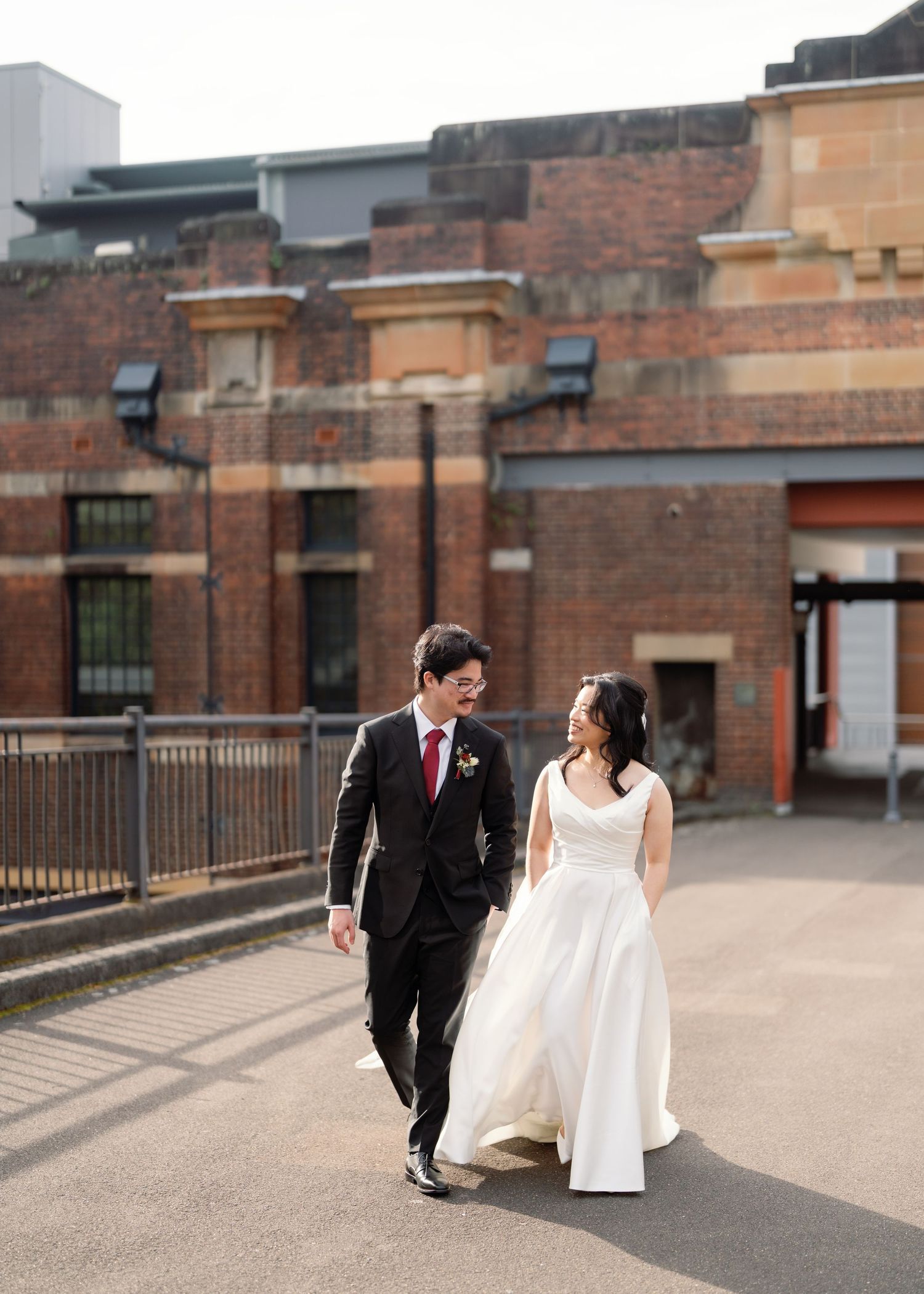 Newlyweds walking together on brick courtyard with urban architecture backdrop.