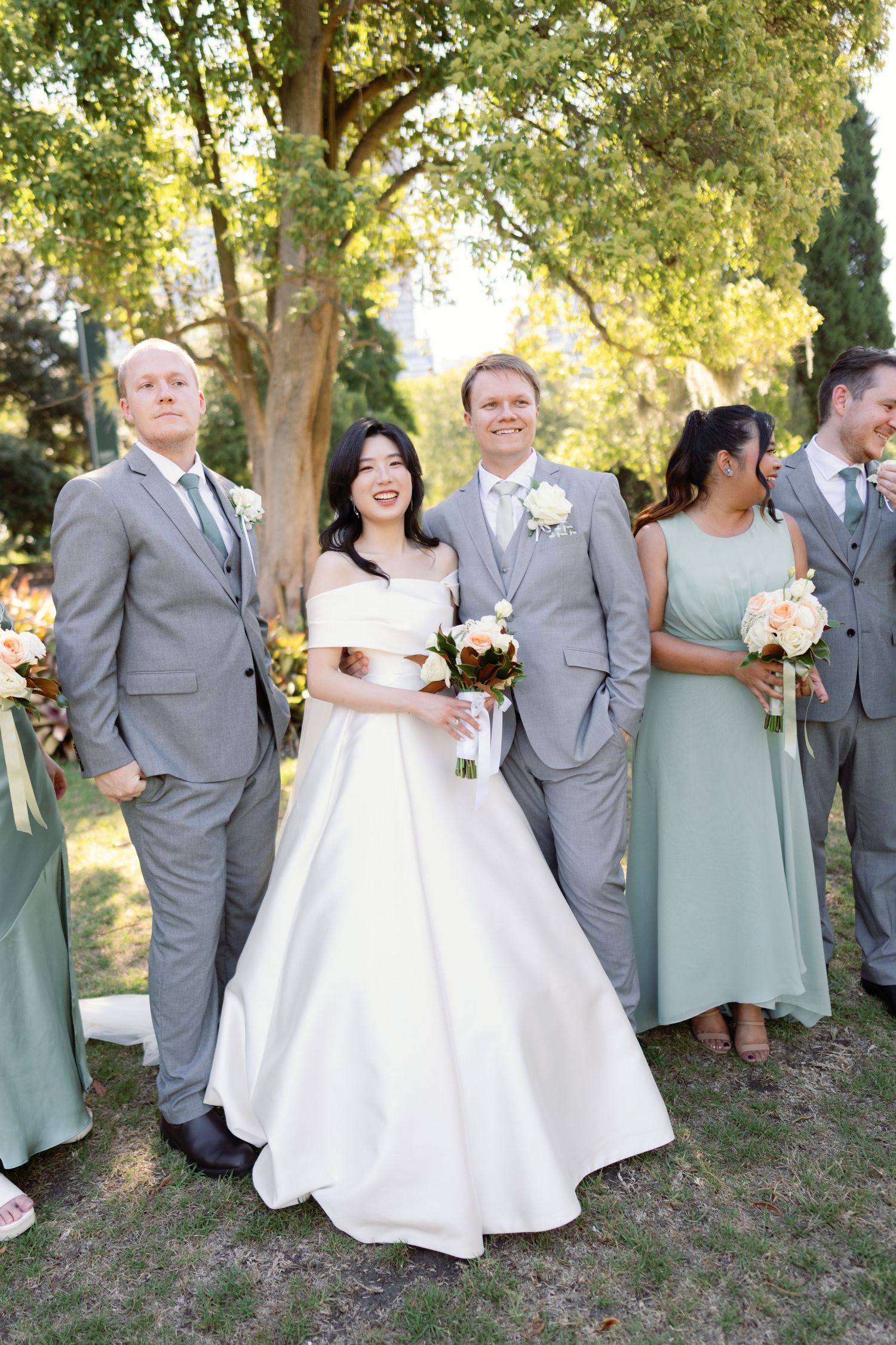Wedding party in gray suits and sage green dresses pose together outdoors.