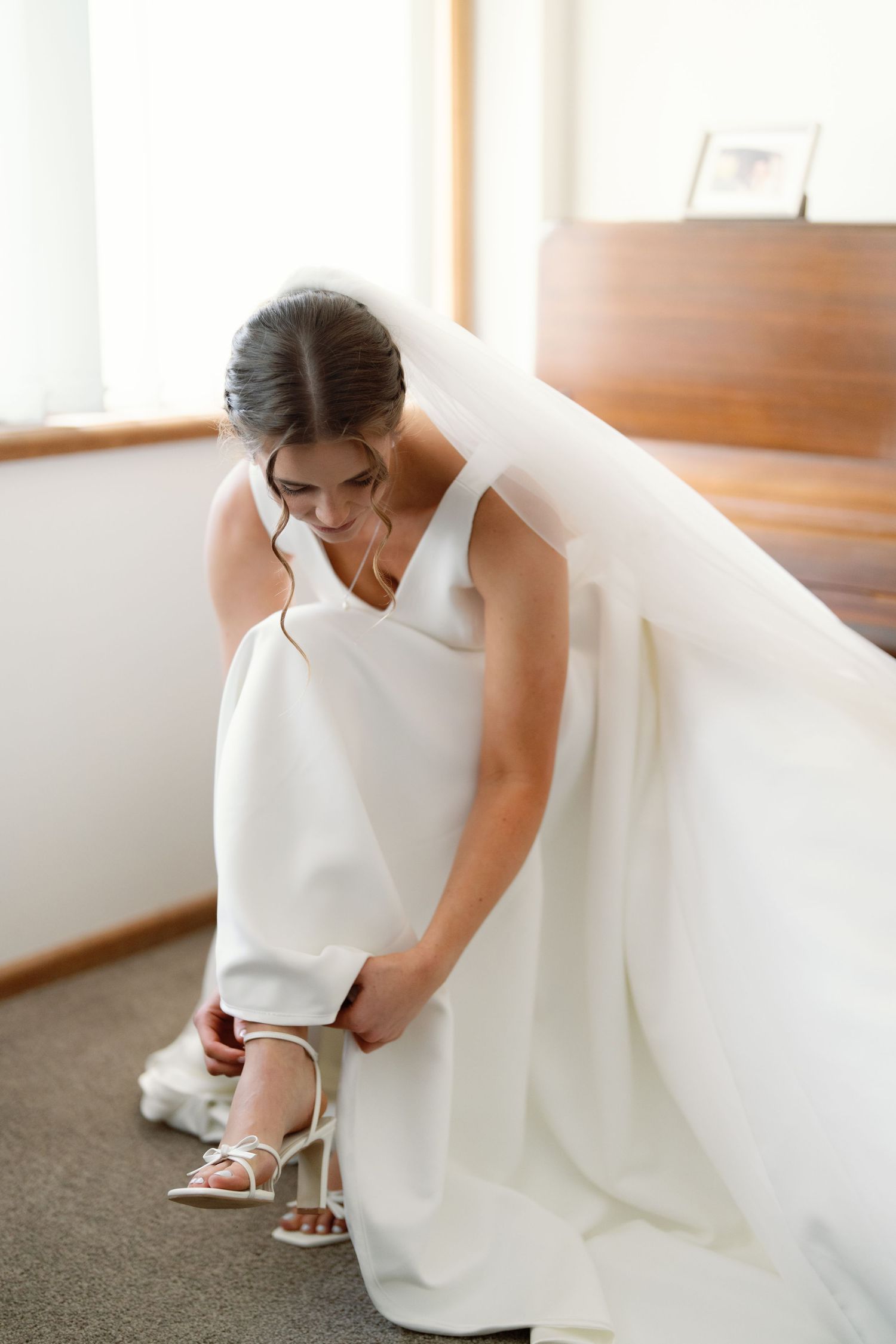 Close-up view of a bride adjusting her white shoe while wearing an elegant wedding dress.