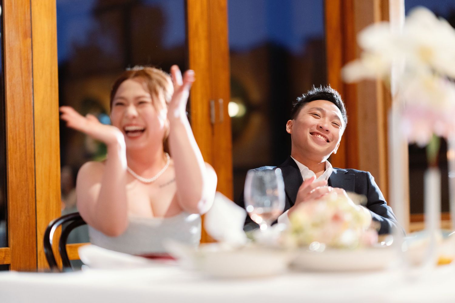 Wedding guests sitting at reception tables raise their hands in celebration during a joyful moment.