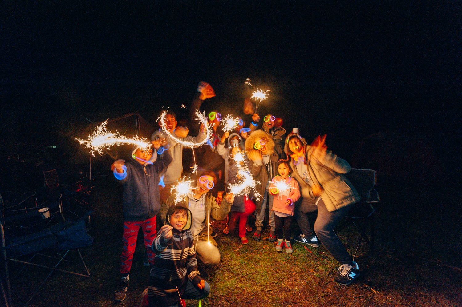 A group holds sparklers while celebrating outdoors at night with a festive atmosphere.