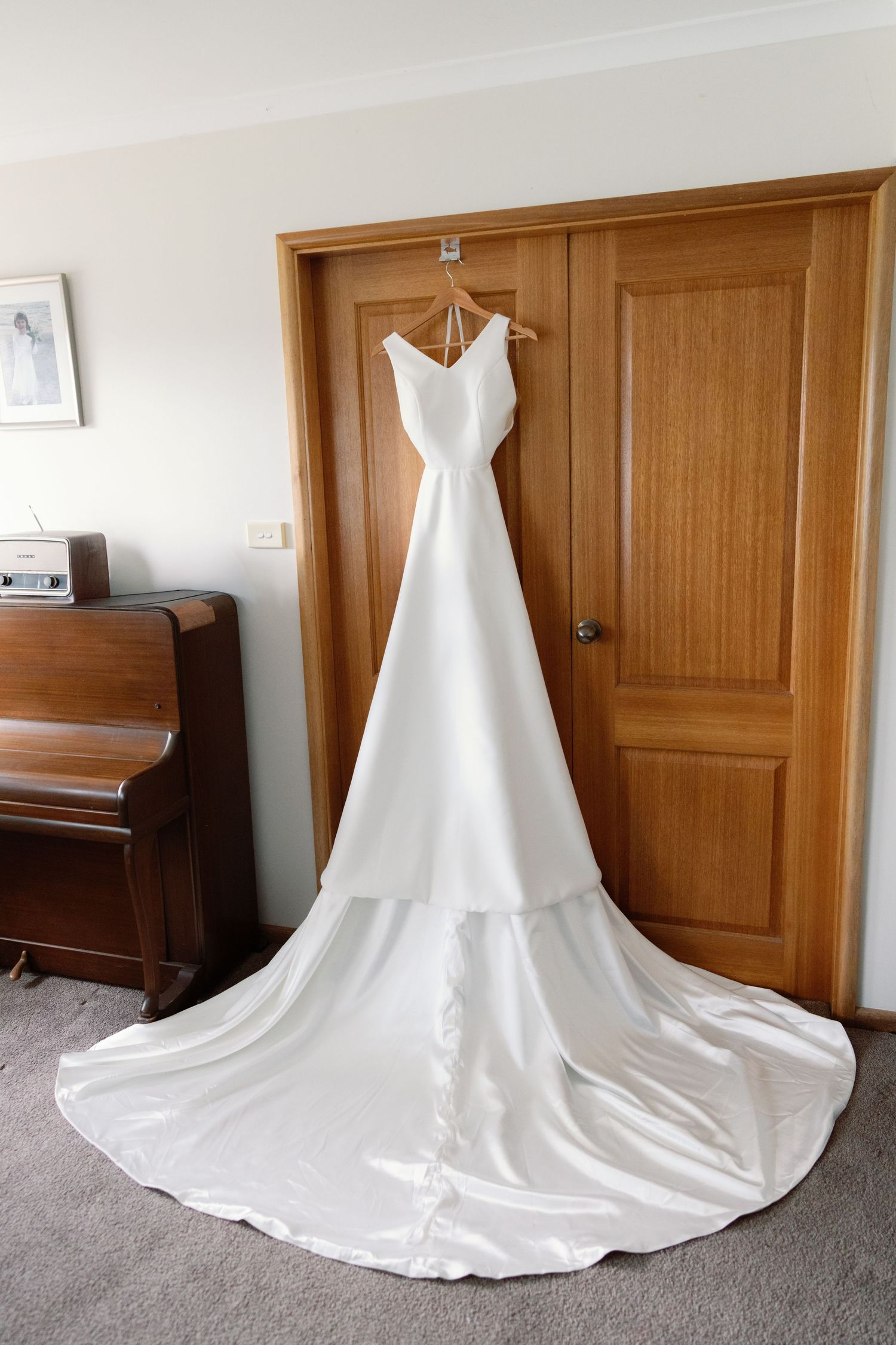 A flowing white wedding dress with long train displayed on carpet against wooden doors.