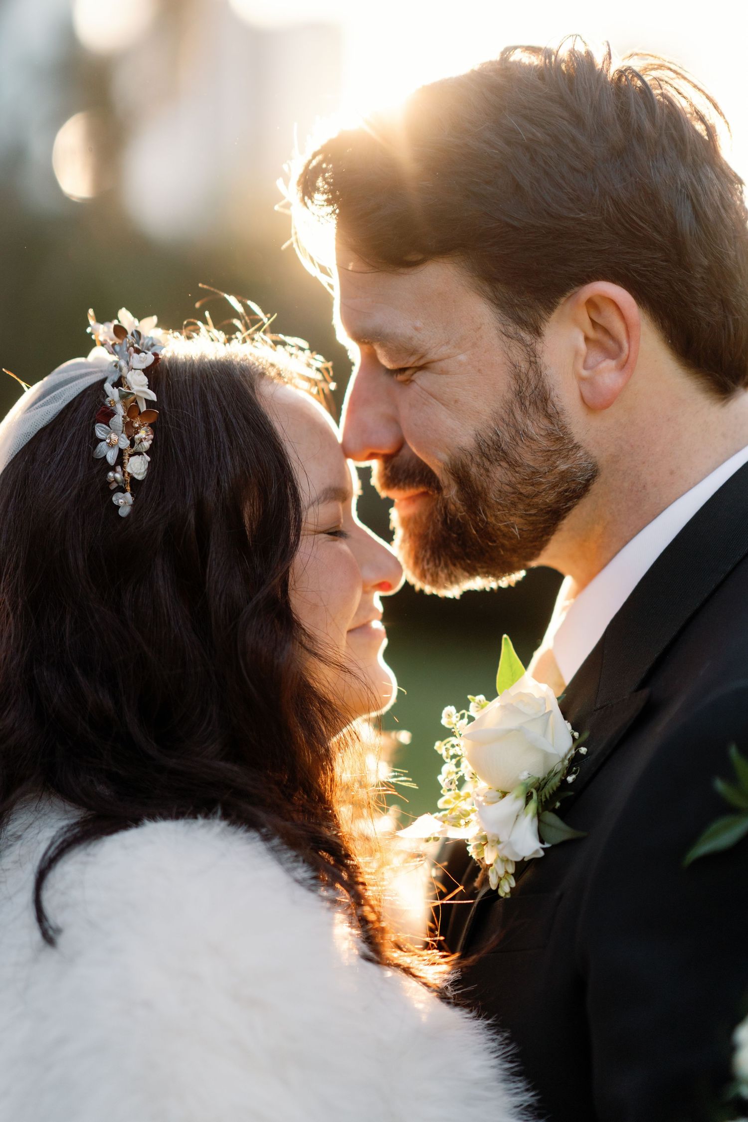 Bride and groom share a romantic moment at golden hour, bride wearing a floral crown and fur wrap.