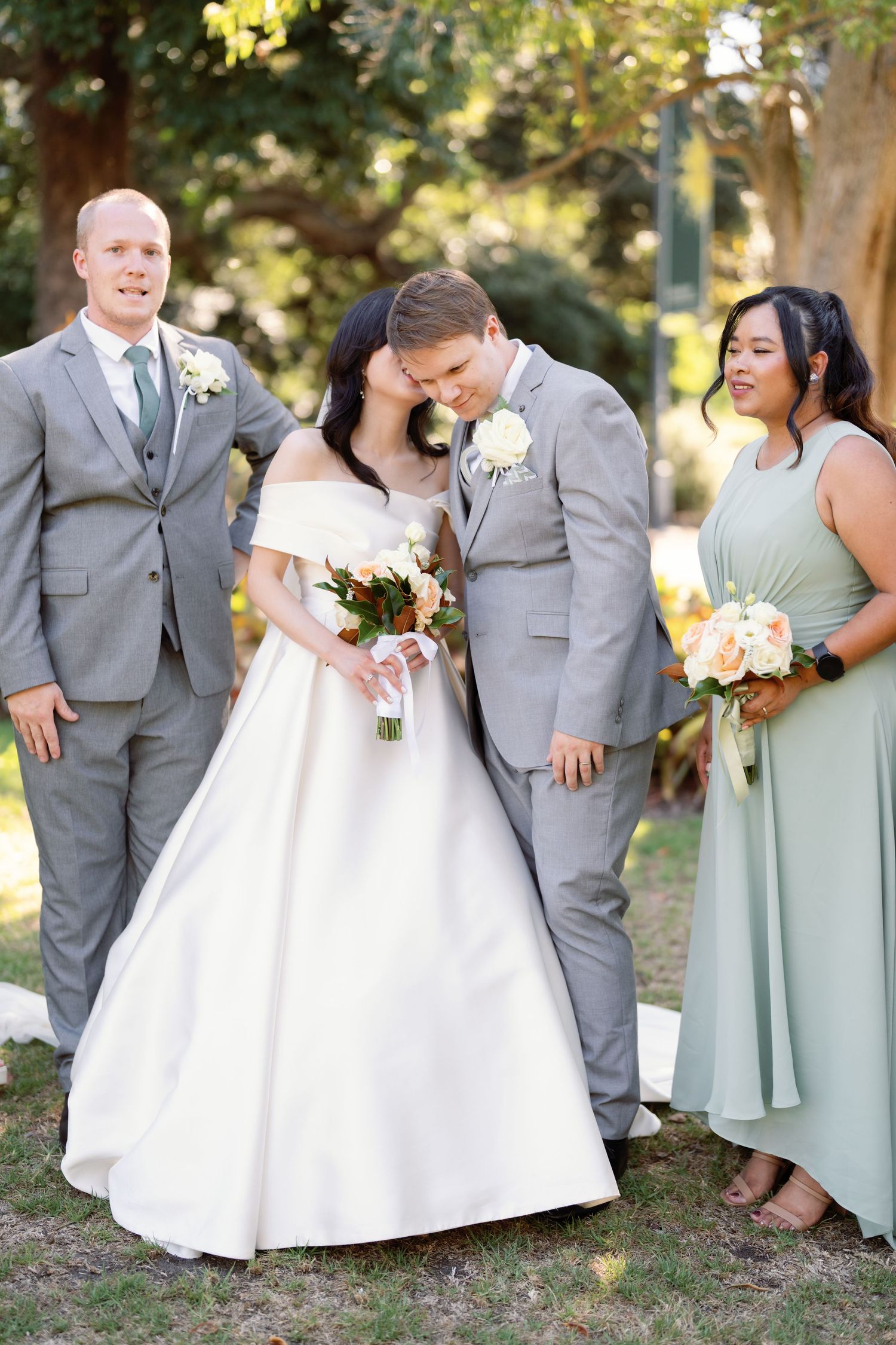 Wedding party in grey suits and mint green dresses posing outdoors.