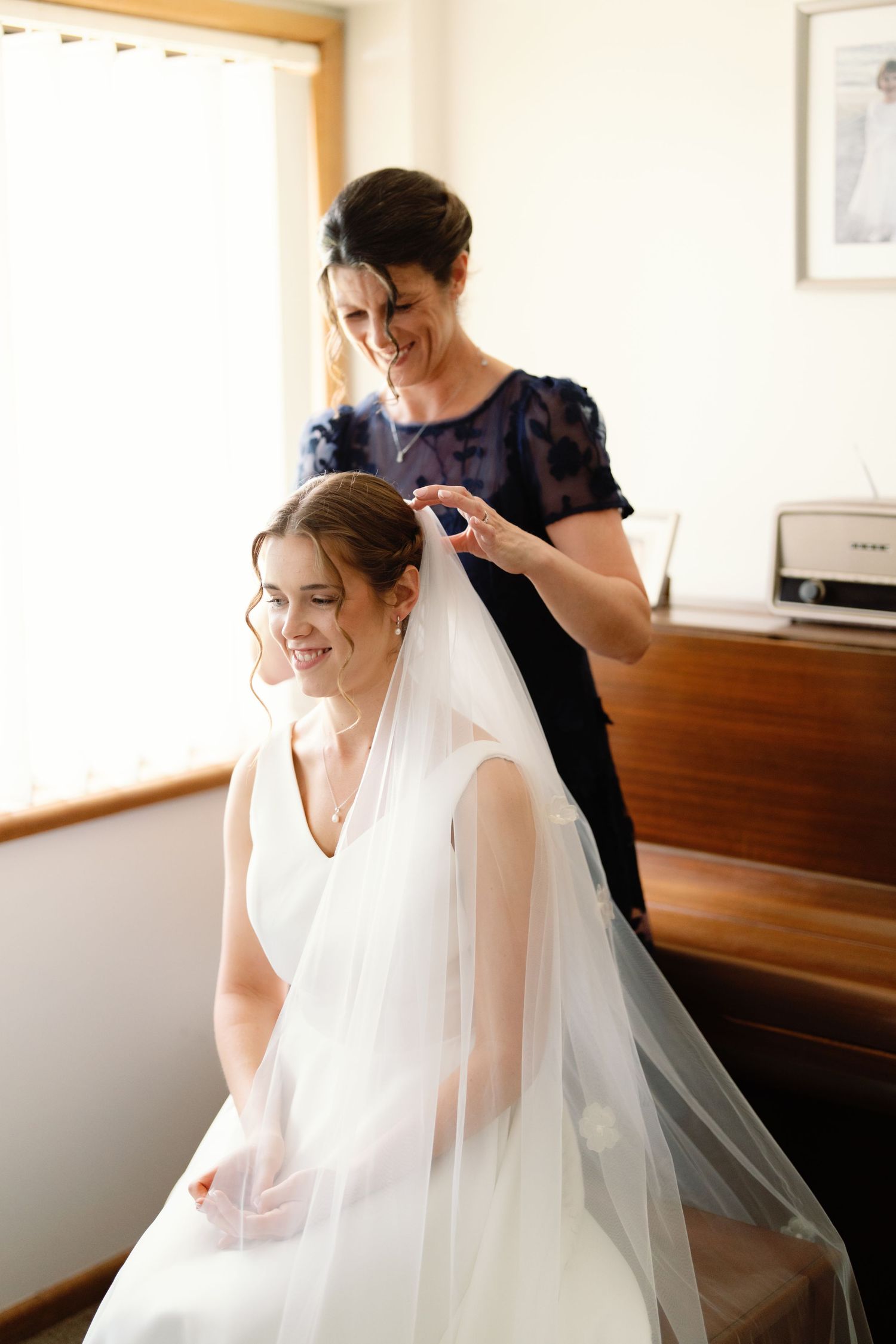 A bride in a white wedding dress gets her veil adjusted during wedding preparations.