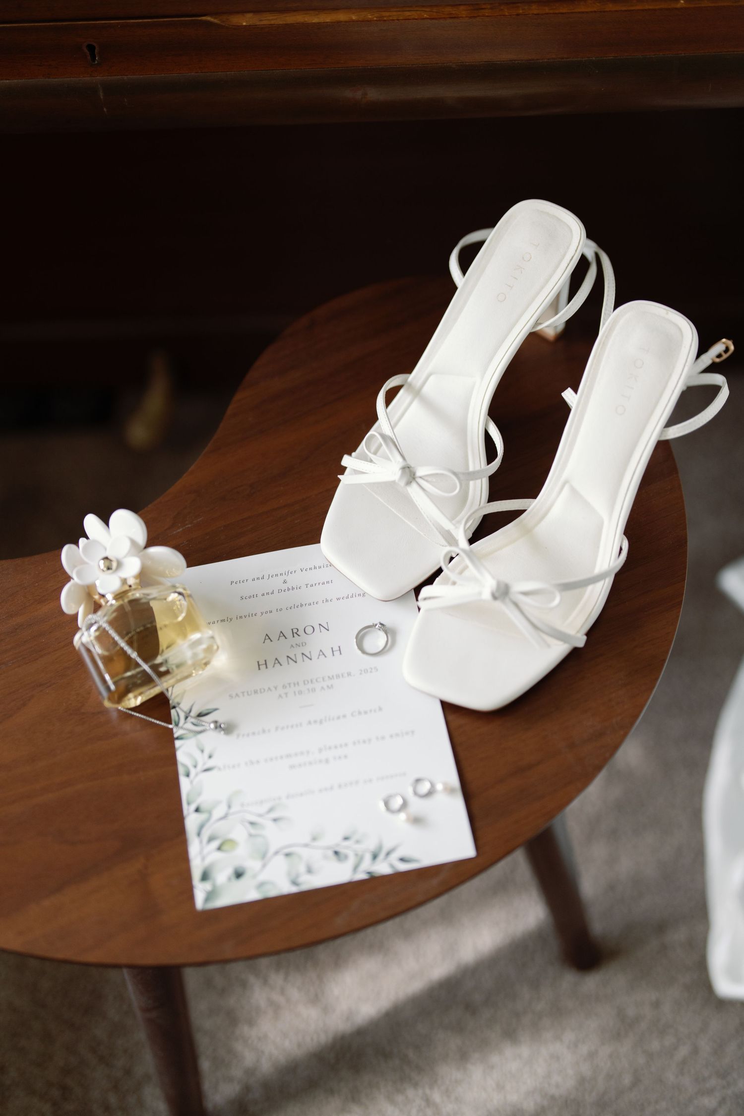 White wedding shoes with delicate floral details rest on a dark wooden surface.