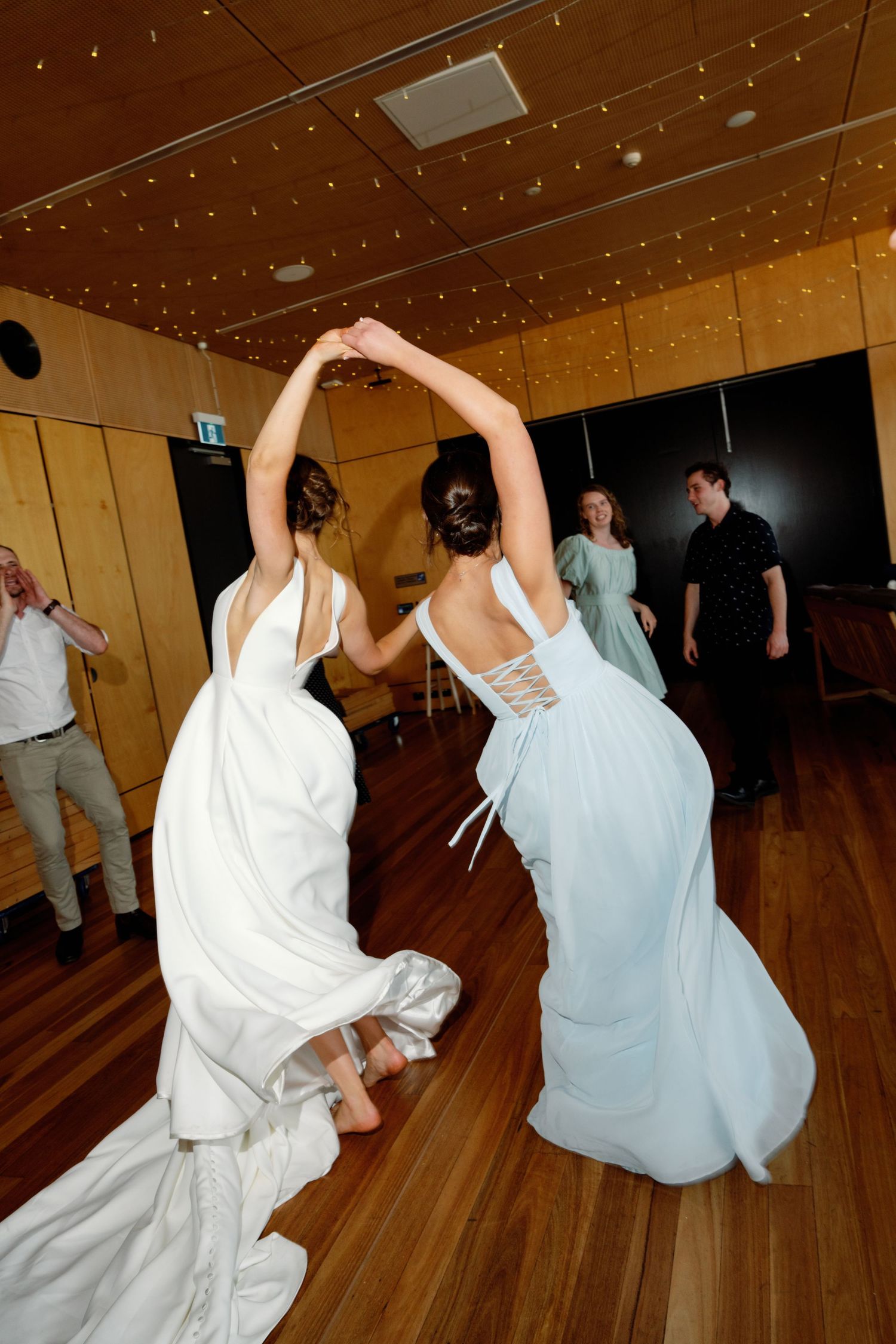 Wedding party members dancing enthusiastically in white and blue attire on wooden dance floor.