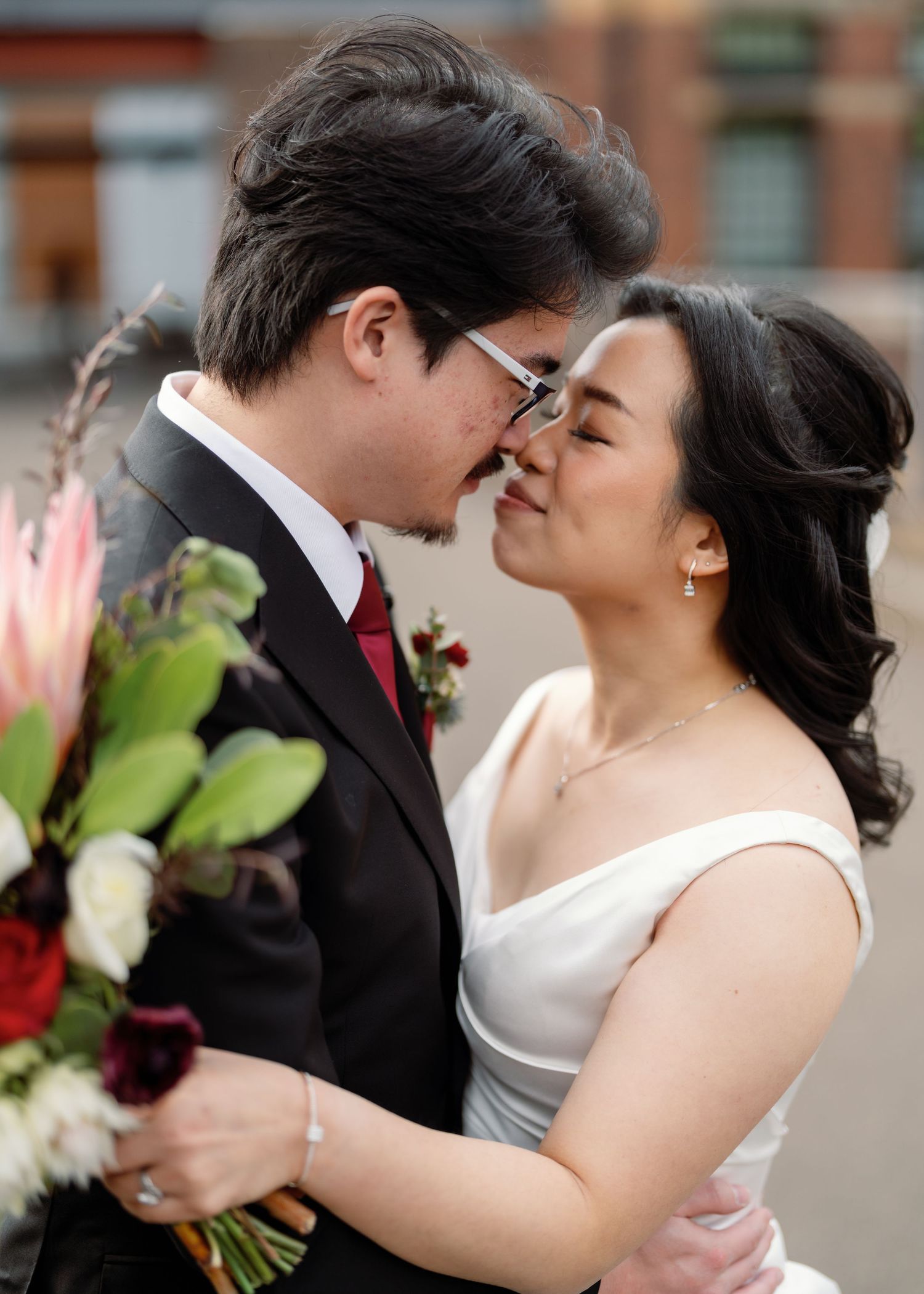A couple shares an intimate moment on their wedding day with red and white bouquet.