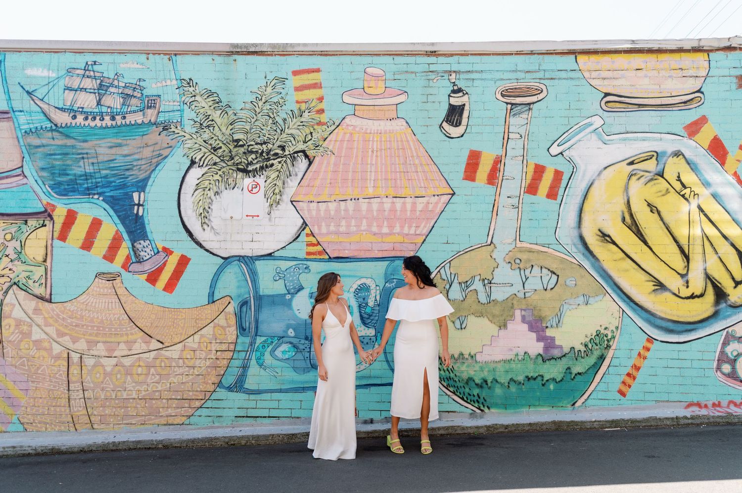 A colorful street mural depicting whimsical scenes with pastel colors and cartoon-style illustrations spans across a long wall.