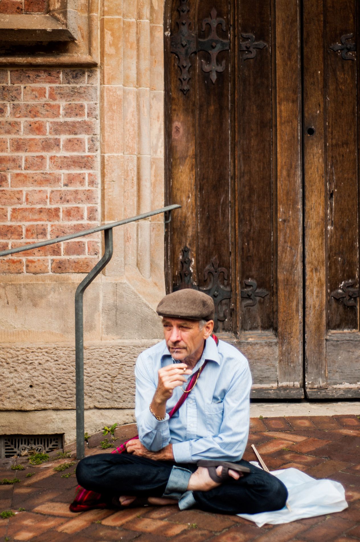 Someone in casual attire sits cross-legged against a historic brick and wooden door entrance.