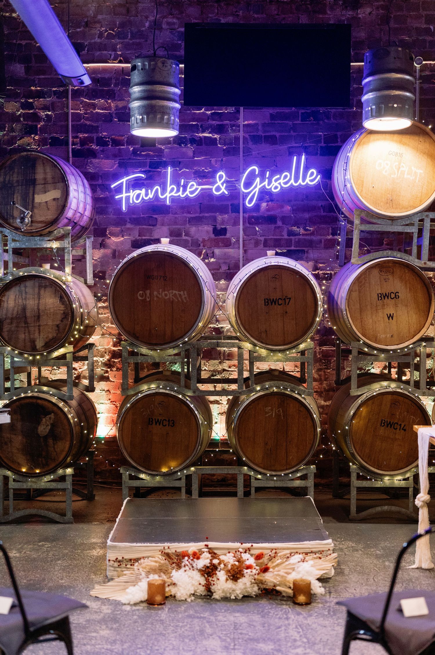 Wine barrels line the brick walls of a rustic venue with purple neon signage and ambient lighting.