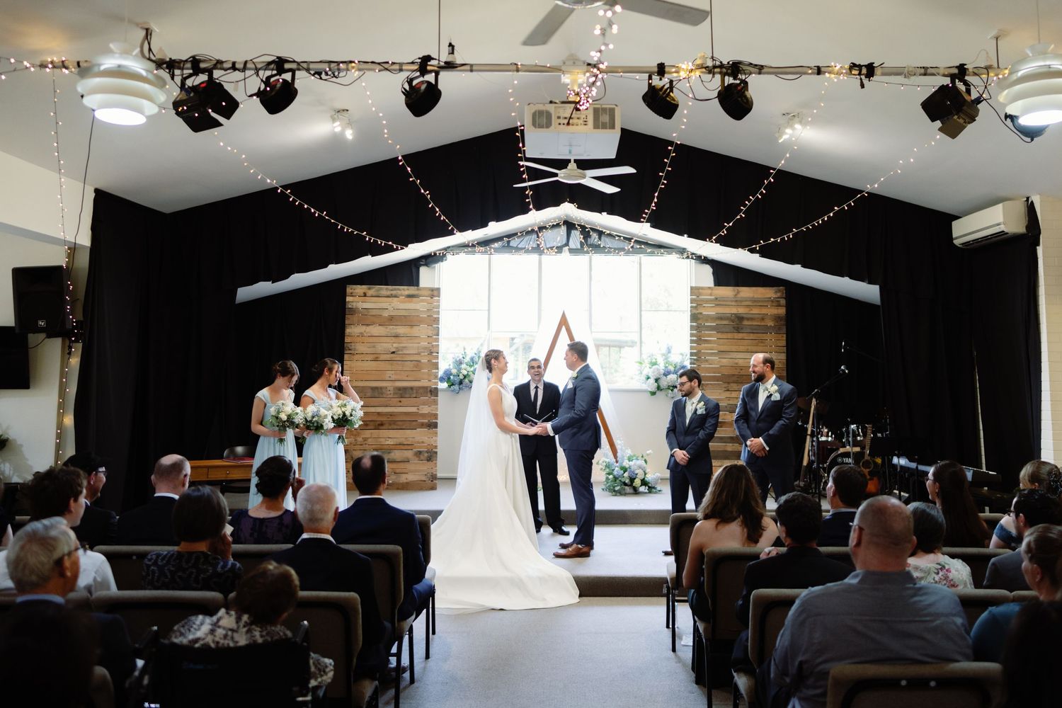 Wedding ceremony venue setup with rows of chairs and stage lighting in an indoor space.