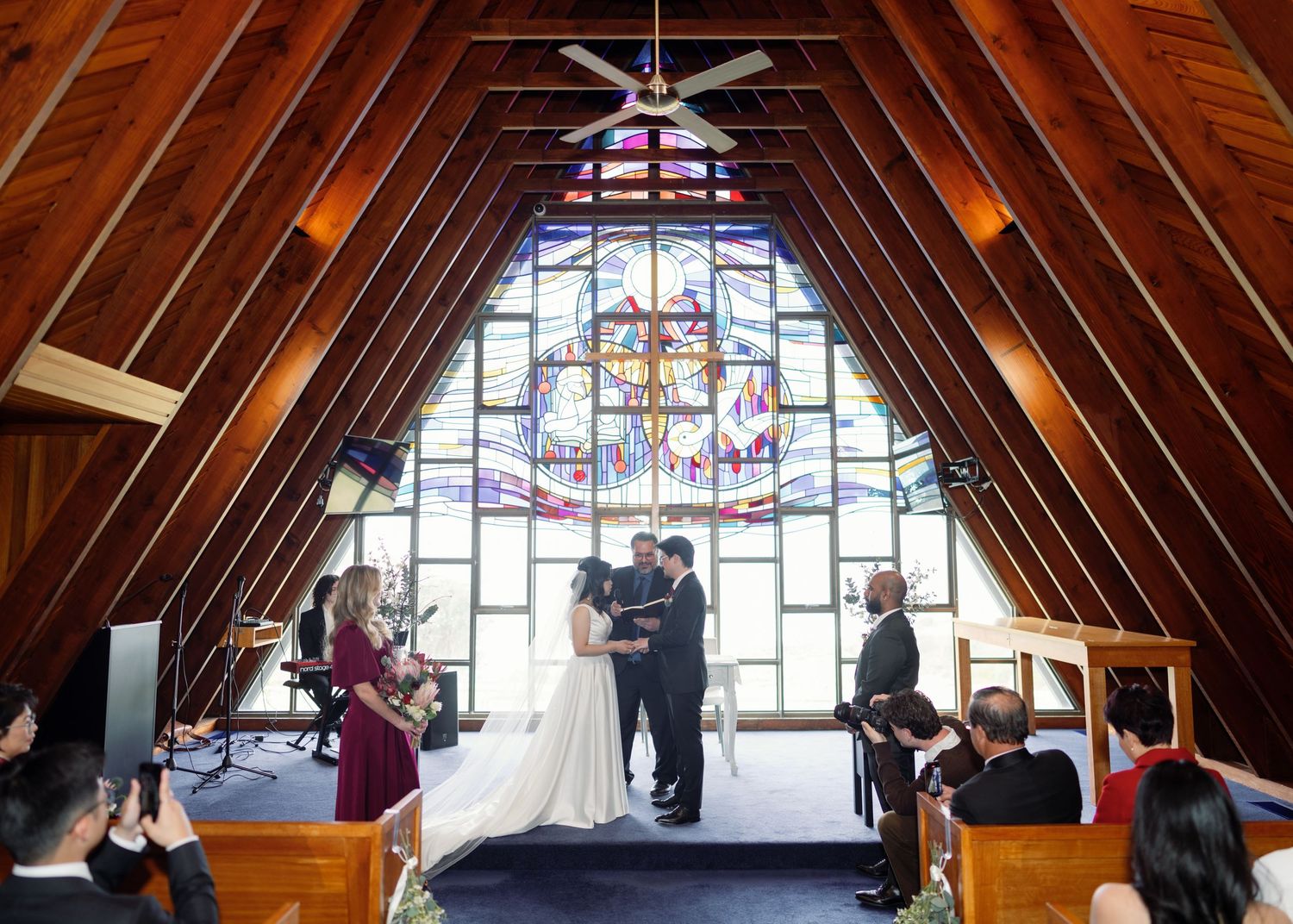 Interior view of an A-frame chapel with dramatic wooden beams and colorful stained glass windows.