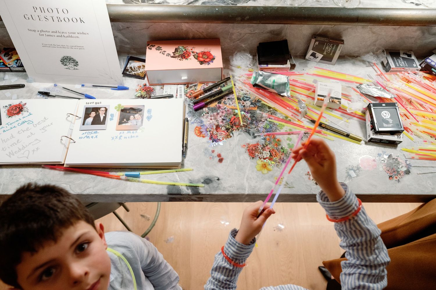 Children create crafts at a wedding photo guestbook activity table filled with colorful supplies.