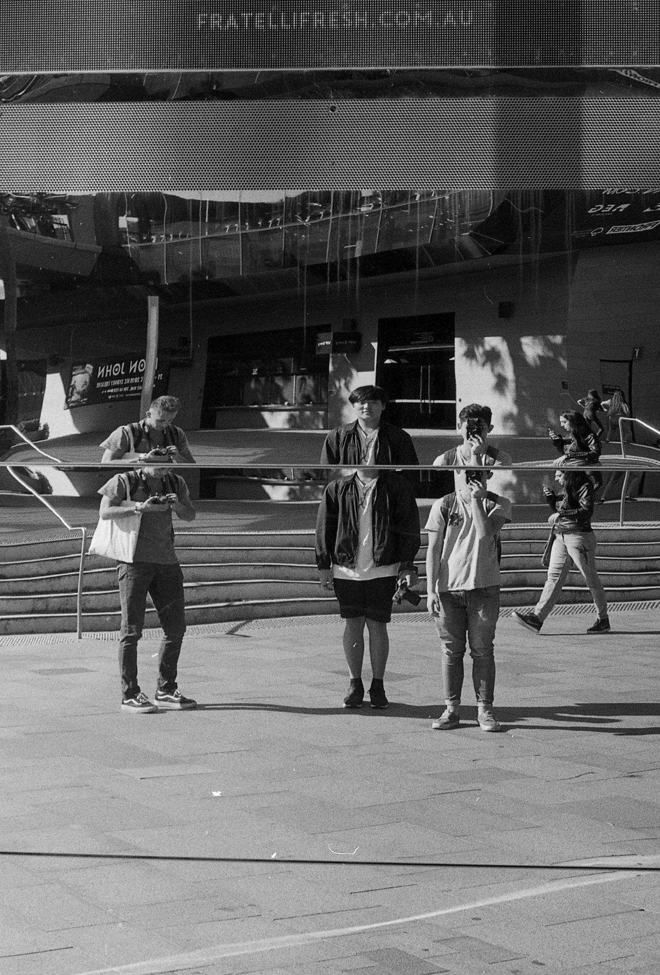 Three people stand in formation on a sunny plaza in black and white.