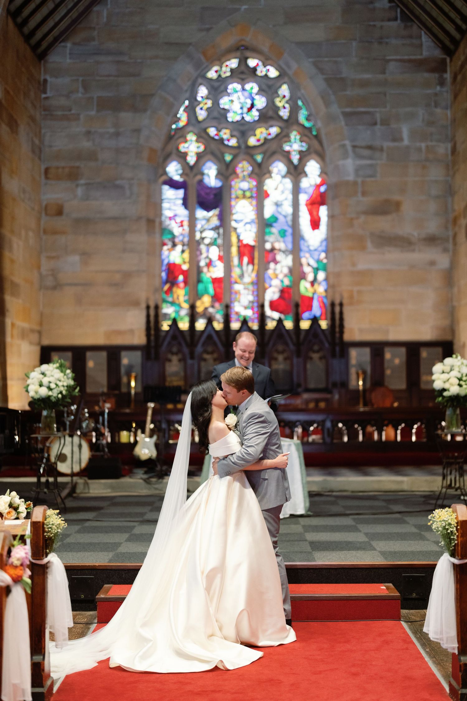 Wedding ceremony setup in stone church with stained glass windows and red carpet aisle.