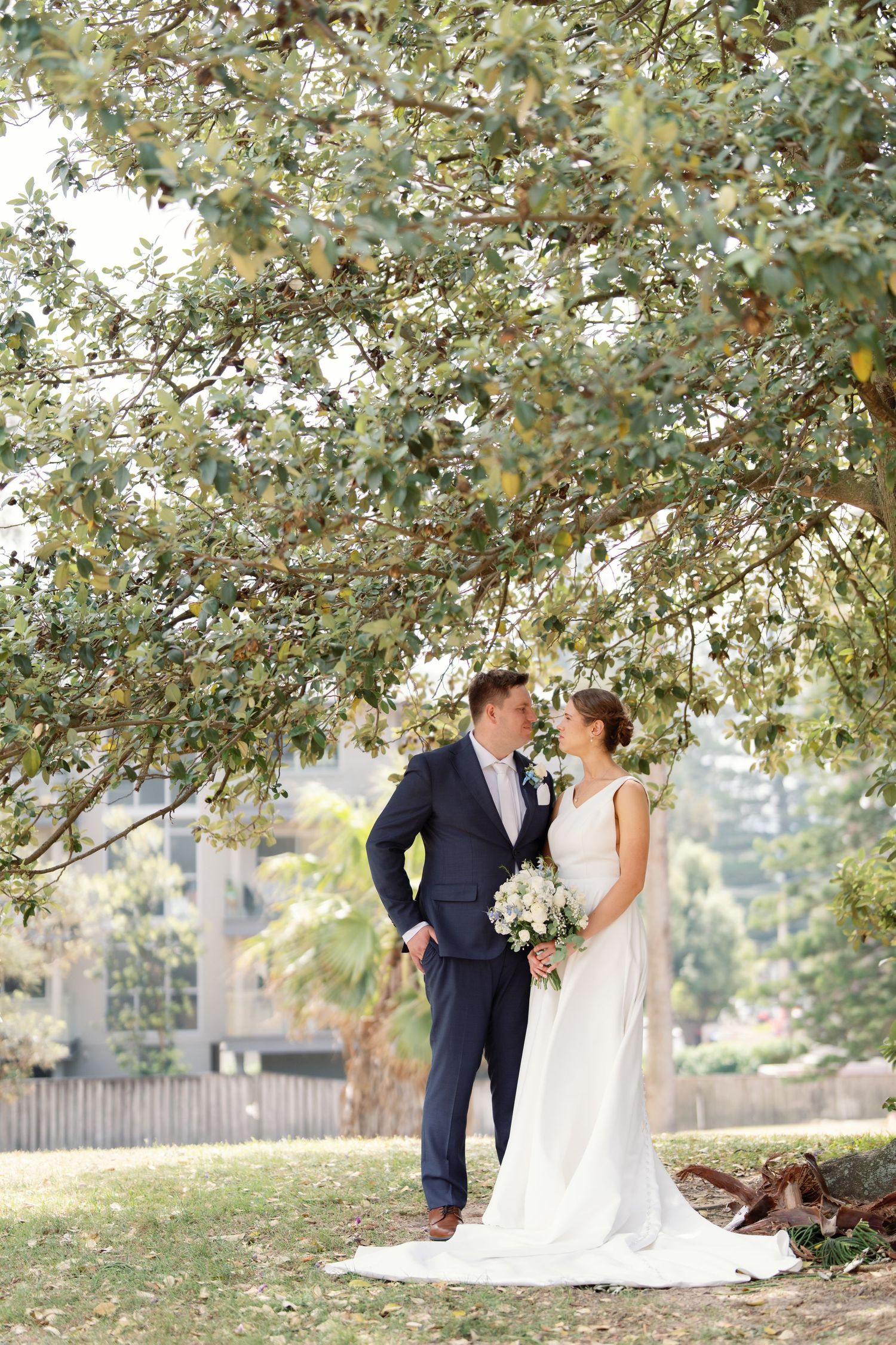 A romantic wedding photo series under a tree with soft natural lighting and greenery in the background.