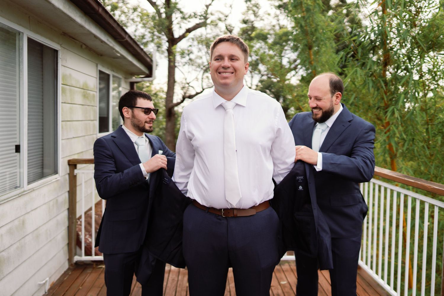 Guests in formal attire gather at an outdoor wedding venue with white railings and greenery in the background.