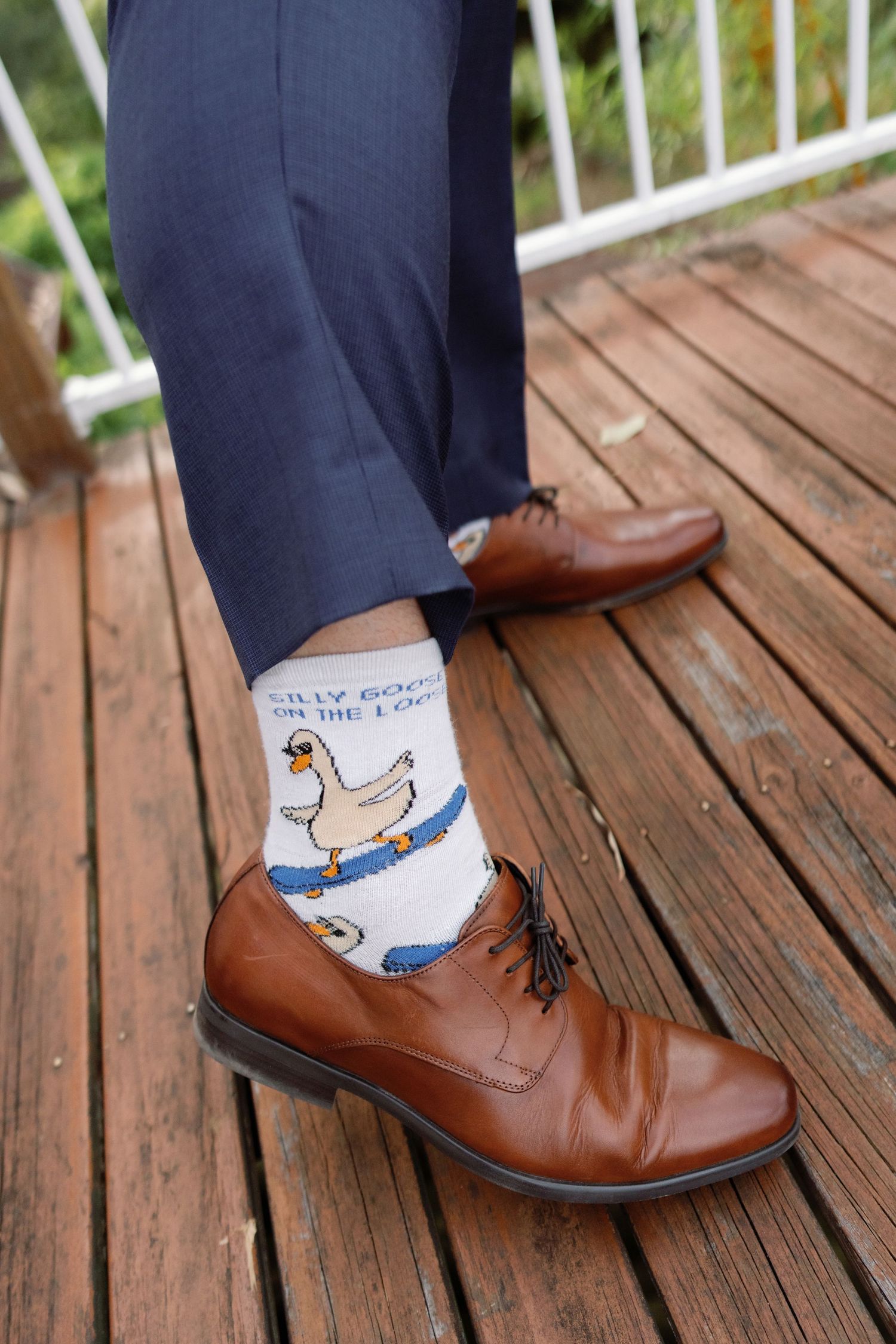 Close-up of brown leather dress shoes paired with fun patterned socks on a wooden deck.