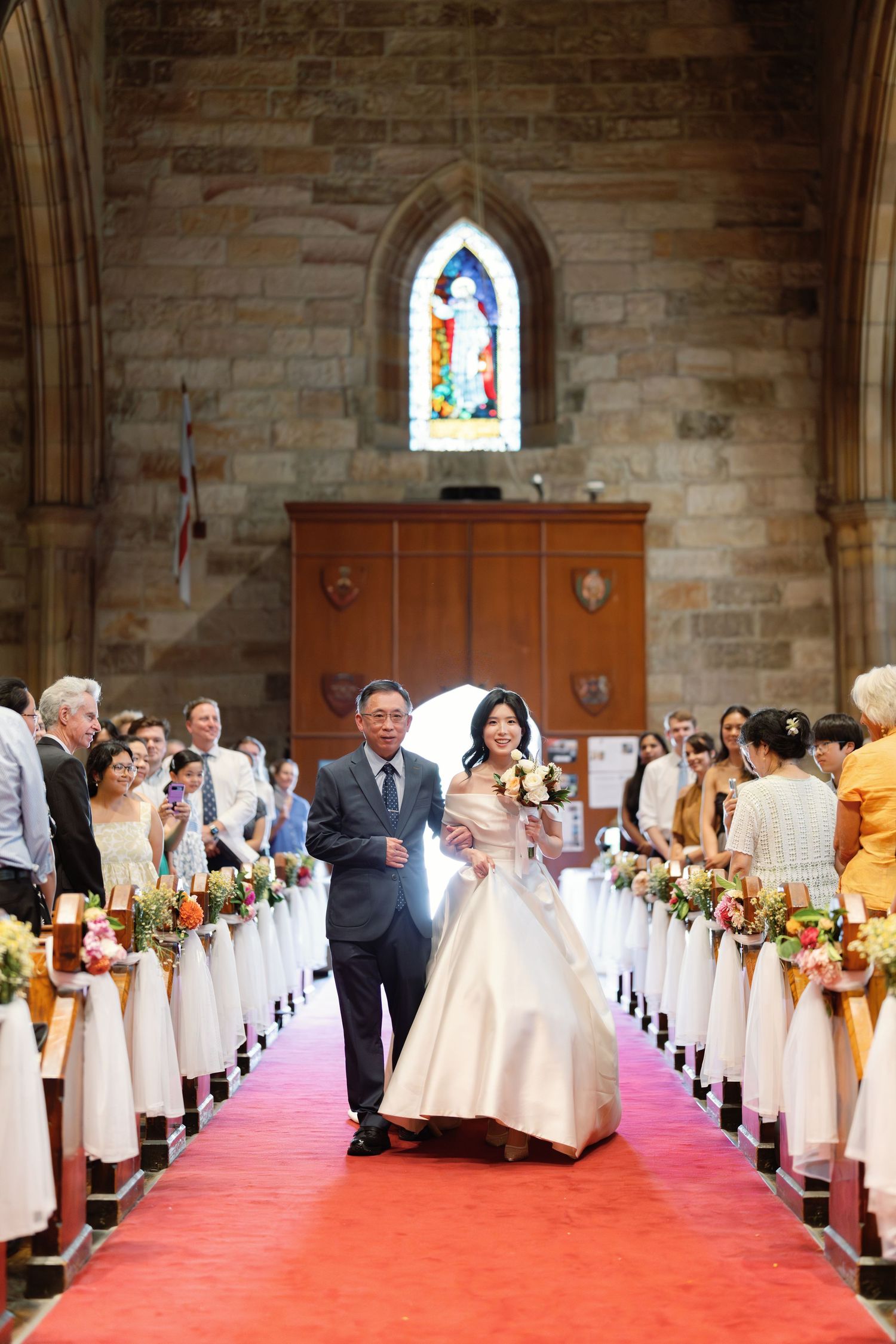 Church interior decorated for wedding ceremony with red carpet aisle and white chair covers.